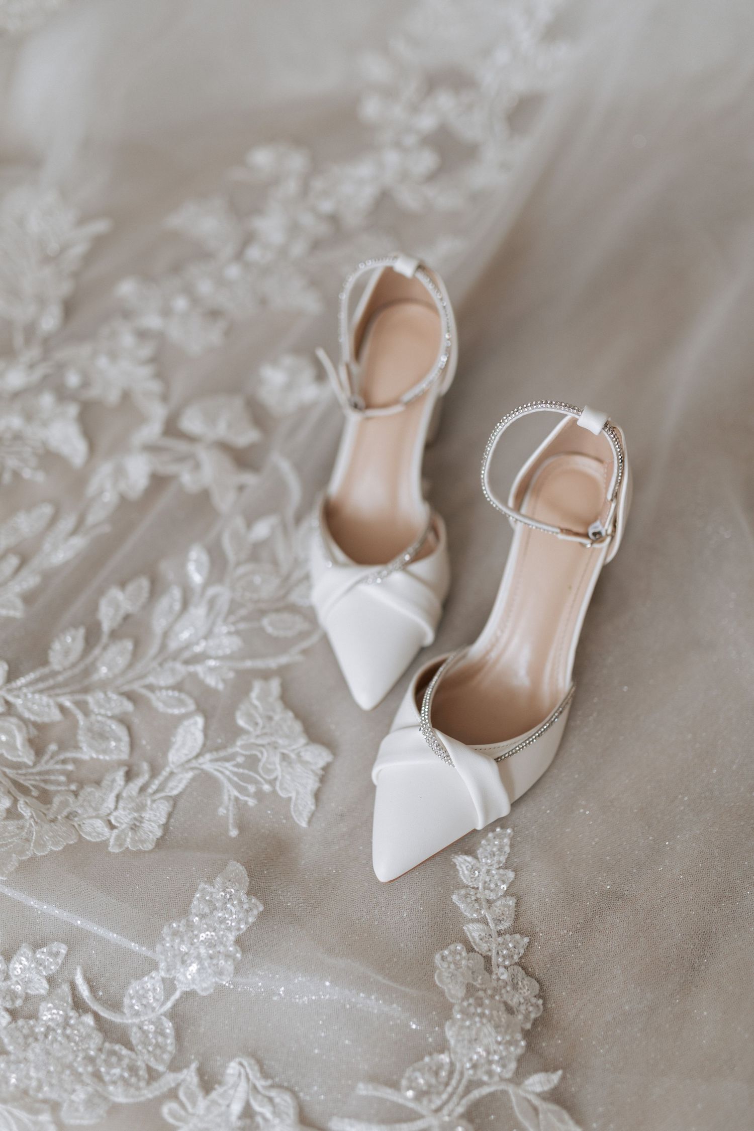 Elegant white pointed-toe bridal shoes placed on delicate lace fabric.