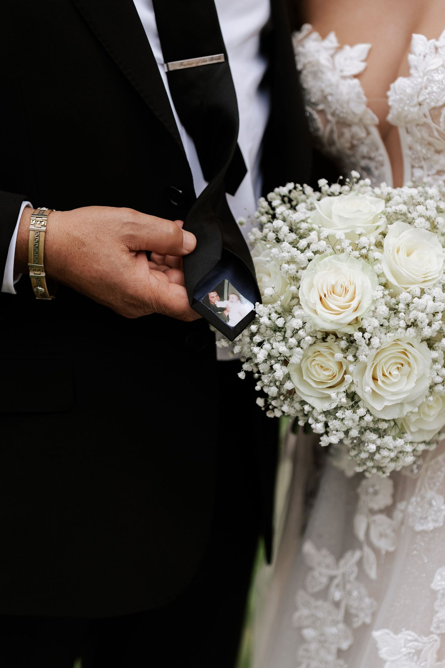 Detail shot of white rose and baby's breath bouquet with groom's formal attire.