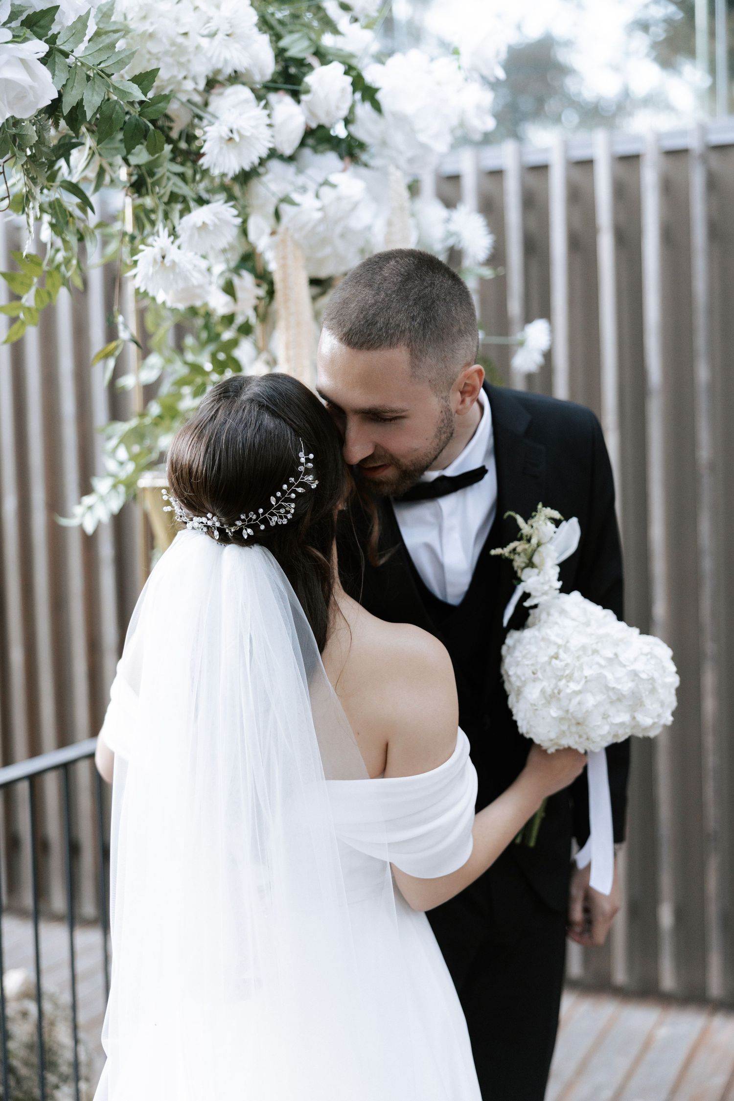 A romantic wedding moment under white floral decorations and greenery.