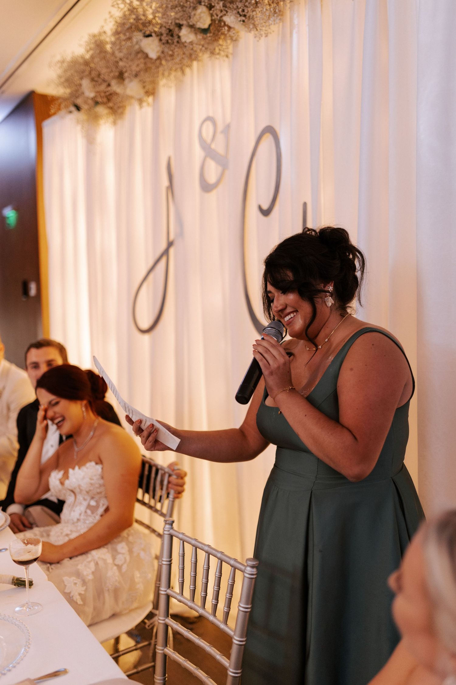 Wedding toast being given at head table with decorative monogram backdrop.