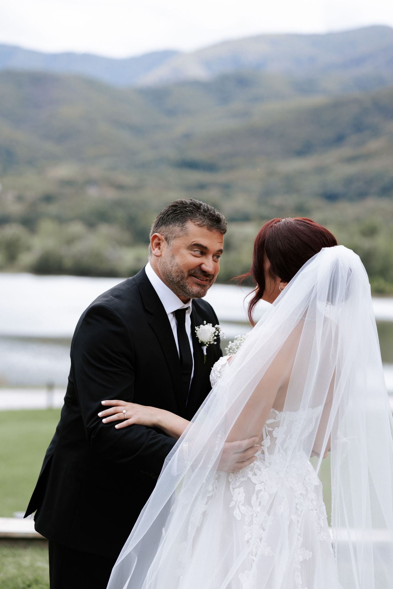 Candid wedding moment captured outdoors with mountains and lake in background.