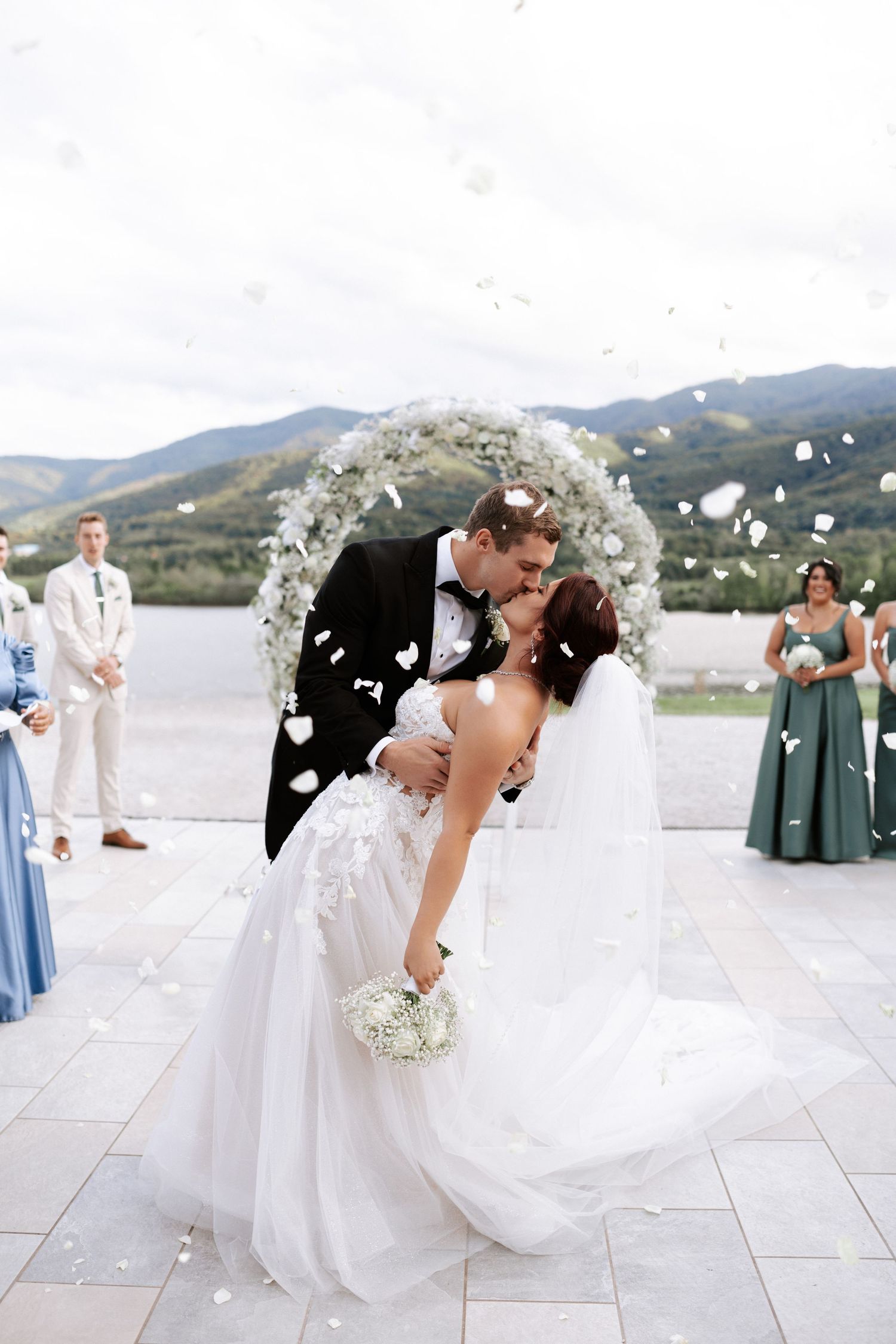 Newlyweds share a romantic kiss under a floral arch at an outdoor mountain venue.Wedding photographer Bulgaria