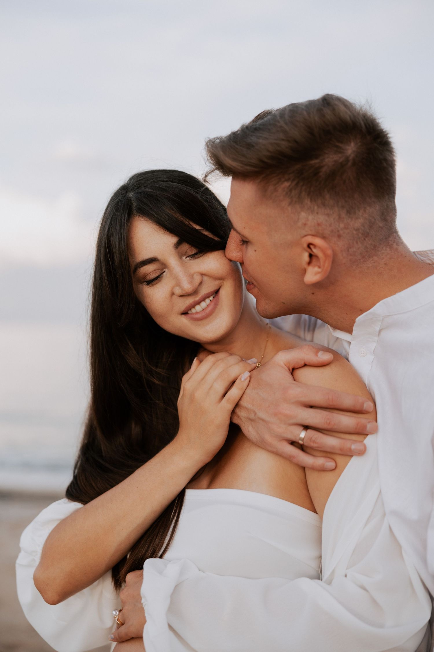 Intimate moment between couple in white clothing on beach at sunset.