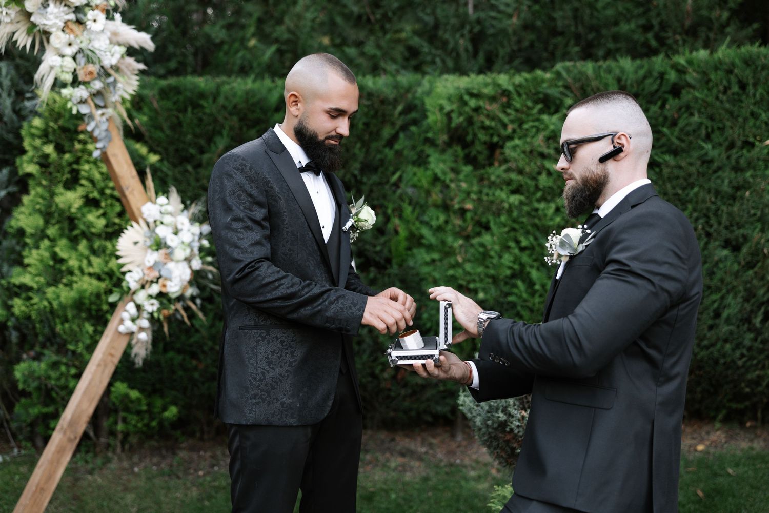 Two people in formal attire share a celebratory toast during an outdoor wedding ceremony.