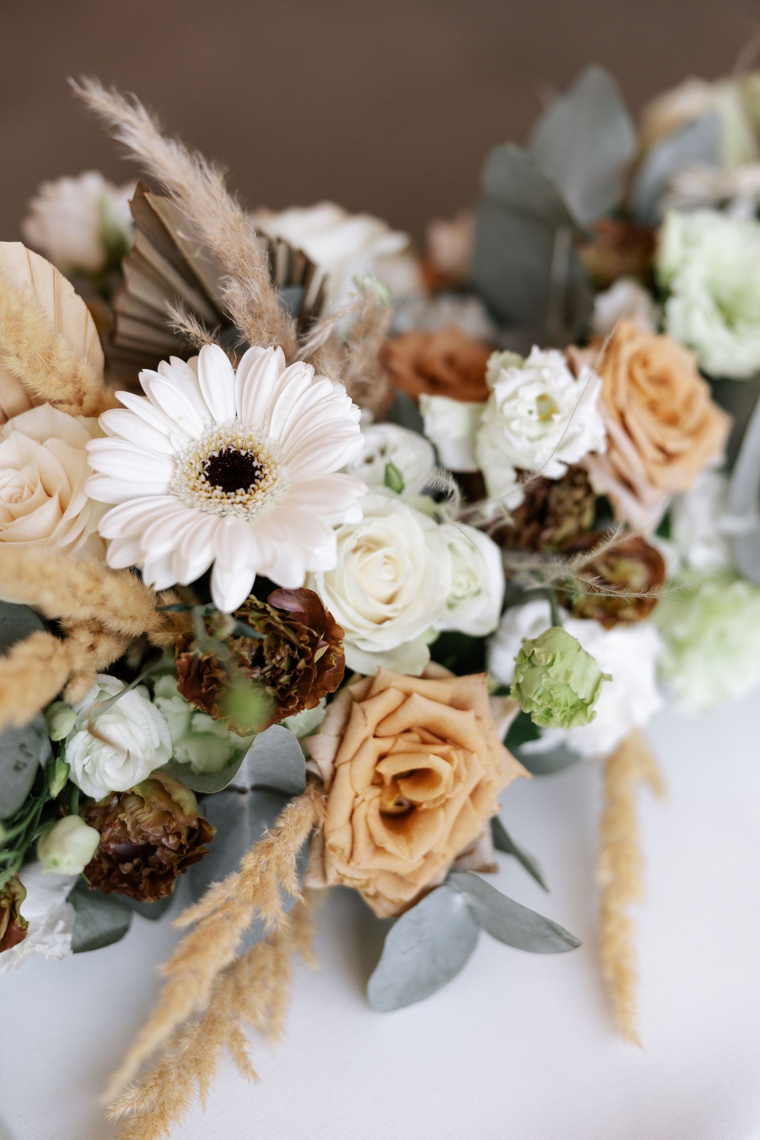 Elegant floral arrangement featuring pale pink roses, white daisies, and dried pampas grass in a soft neutral color palette.