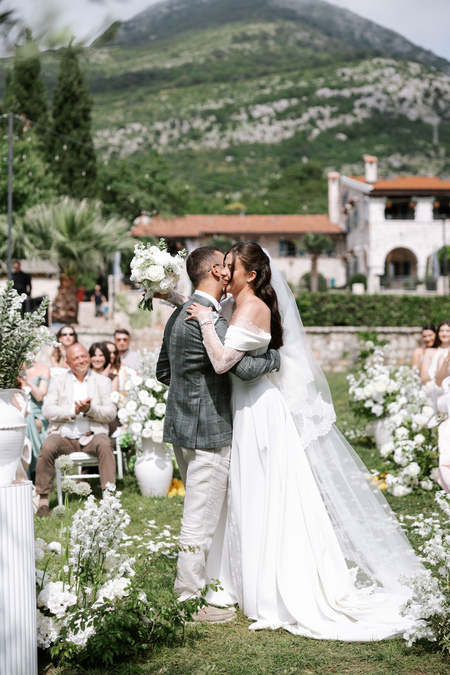 A romantic wedding ceremony sequence in a garden setting with white floral decorations and mountain views in the background.