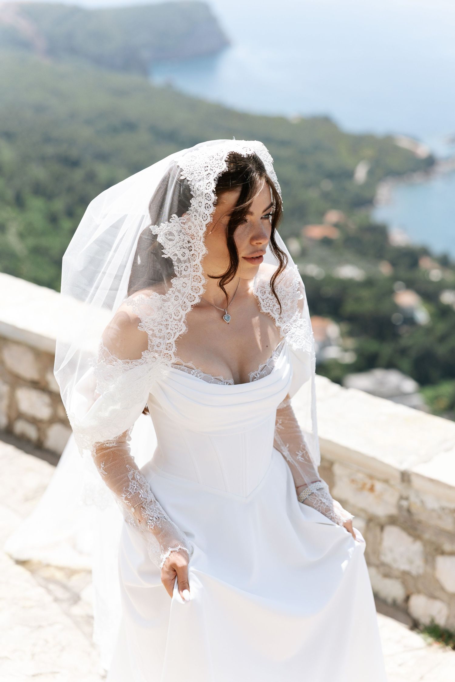 Bride in a lace white wedding dress twirls against a coastal Mediterranean backdrop.