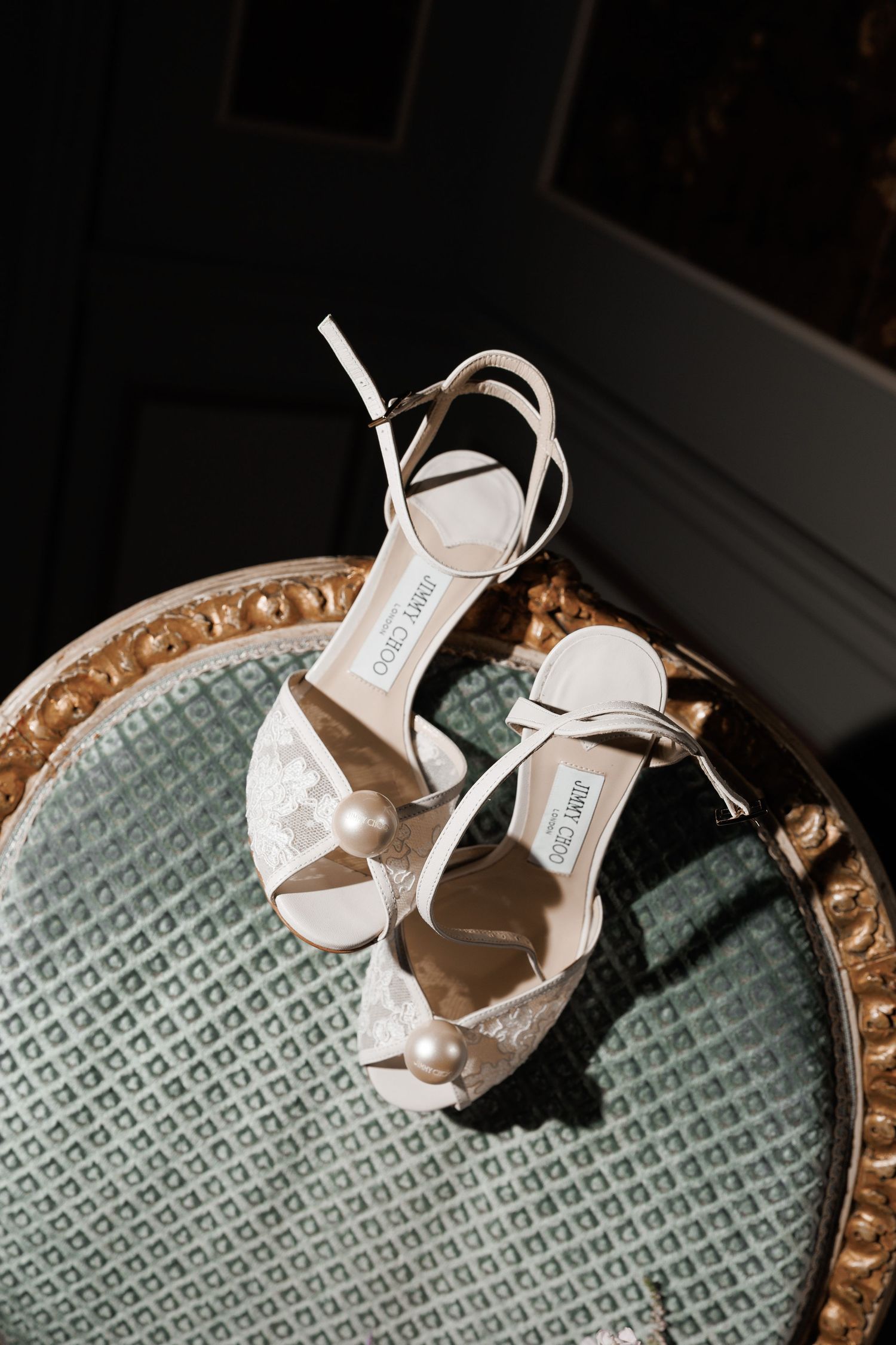 Elegant white bridal sandals with ankle straps photographed on a teal textured surface with dramatic lighting.