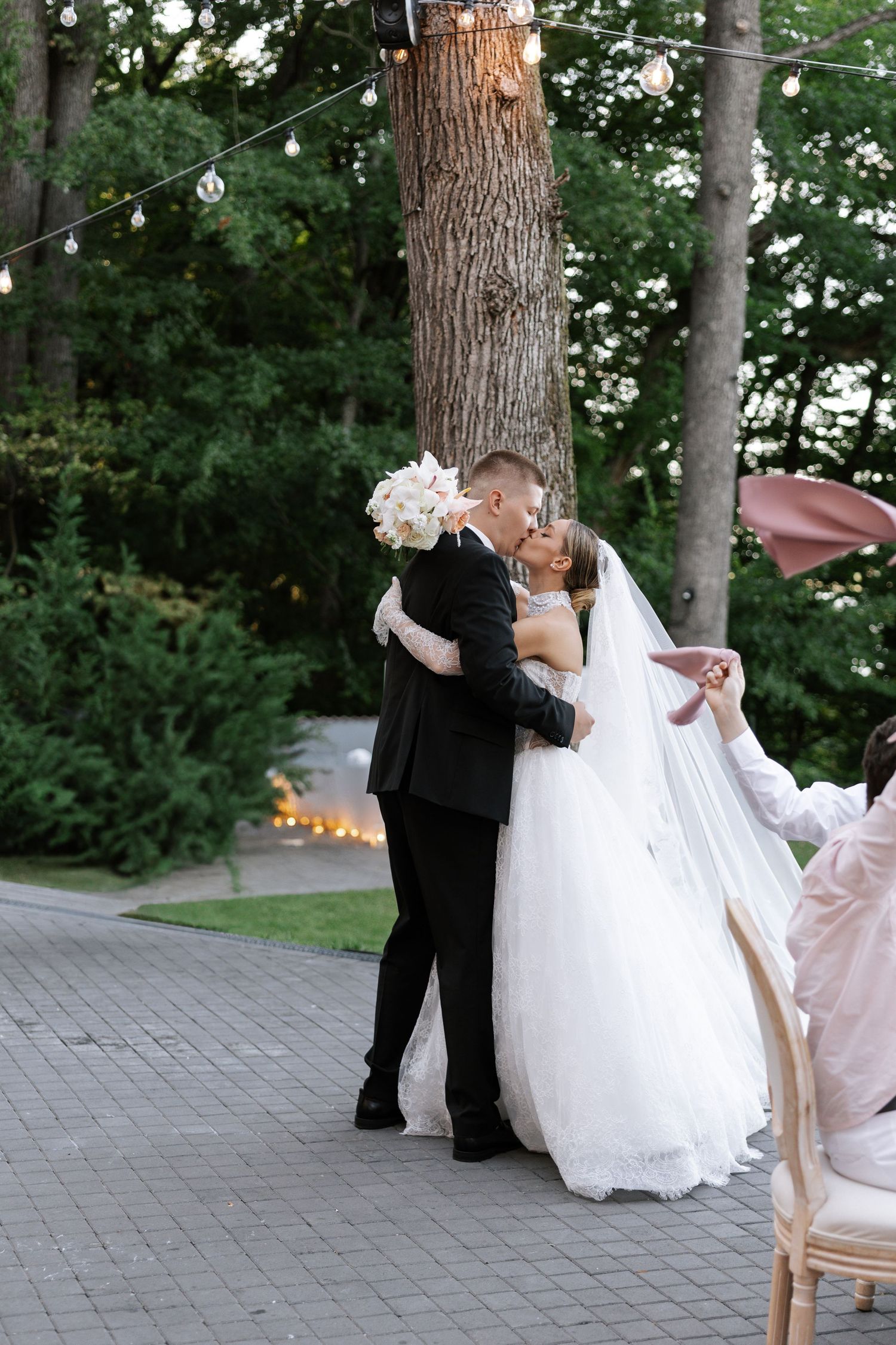 Romantic moment captured under string lights and trees during an outdoor wedding celebration.