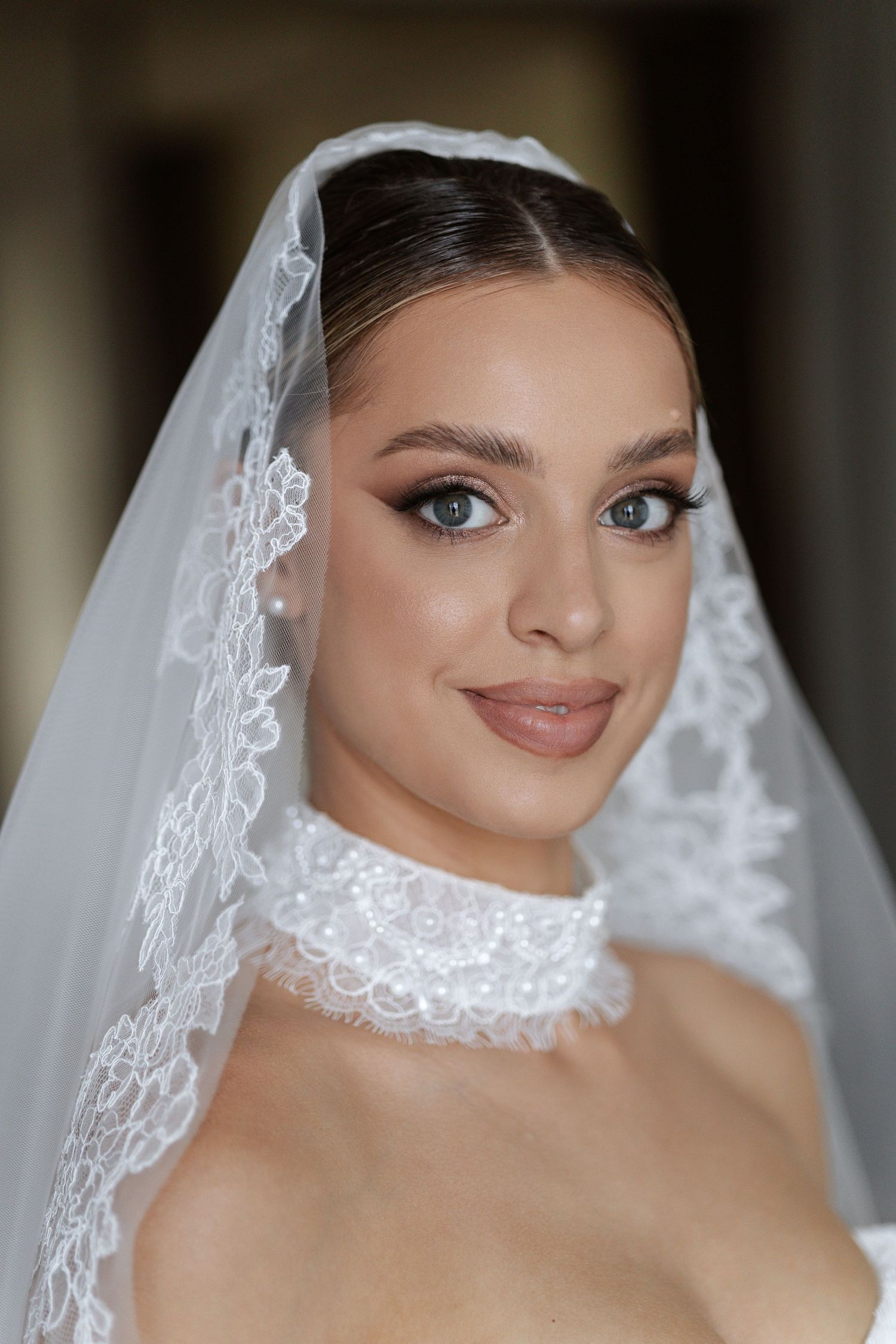 Close-up portrait showing delicate lace veil and bridal makeup.