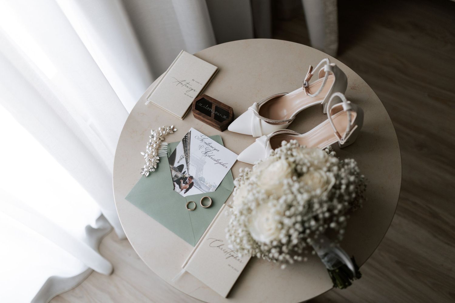 Bridal details flat lay featuring invitation, white shoes and baby's breath on light surface.