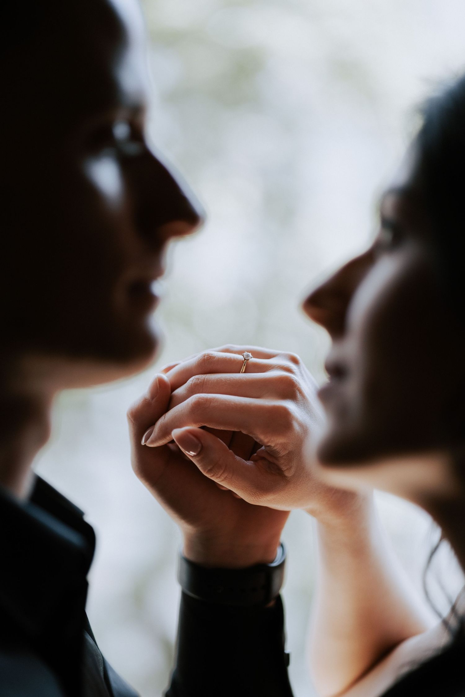 Close up silhouette of couple's hands and faces in tender moment by window.