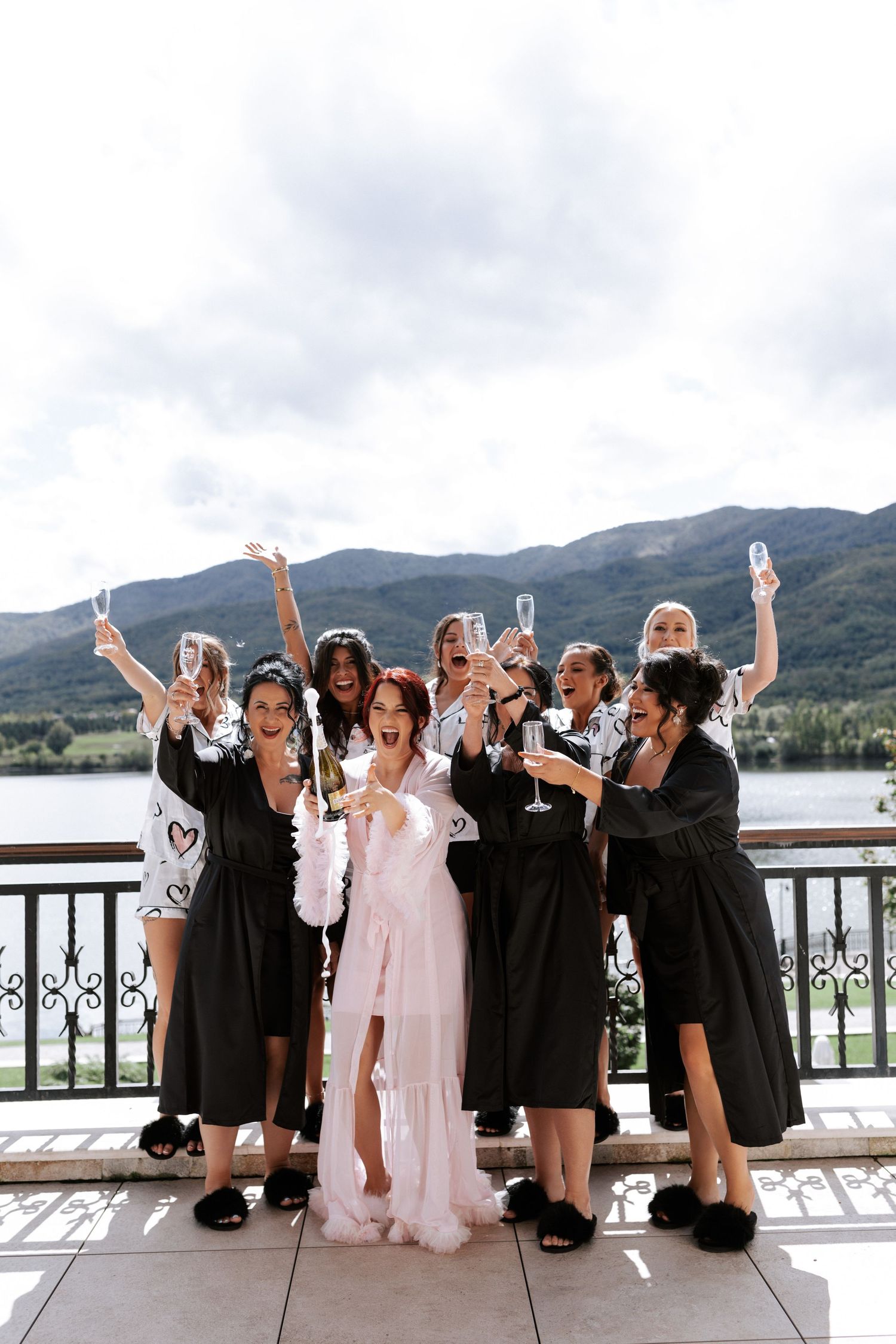 Celebratory group photo with people in black robes and one in pink dress on scenic balcony.
