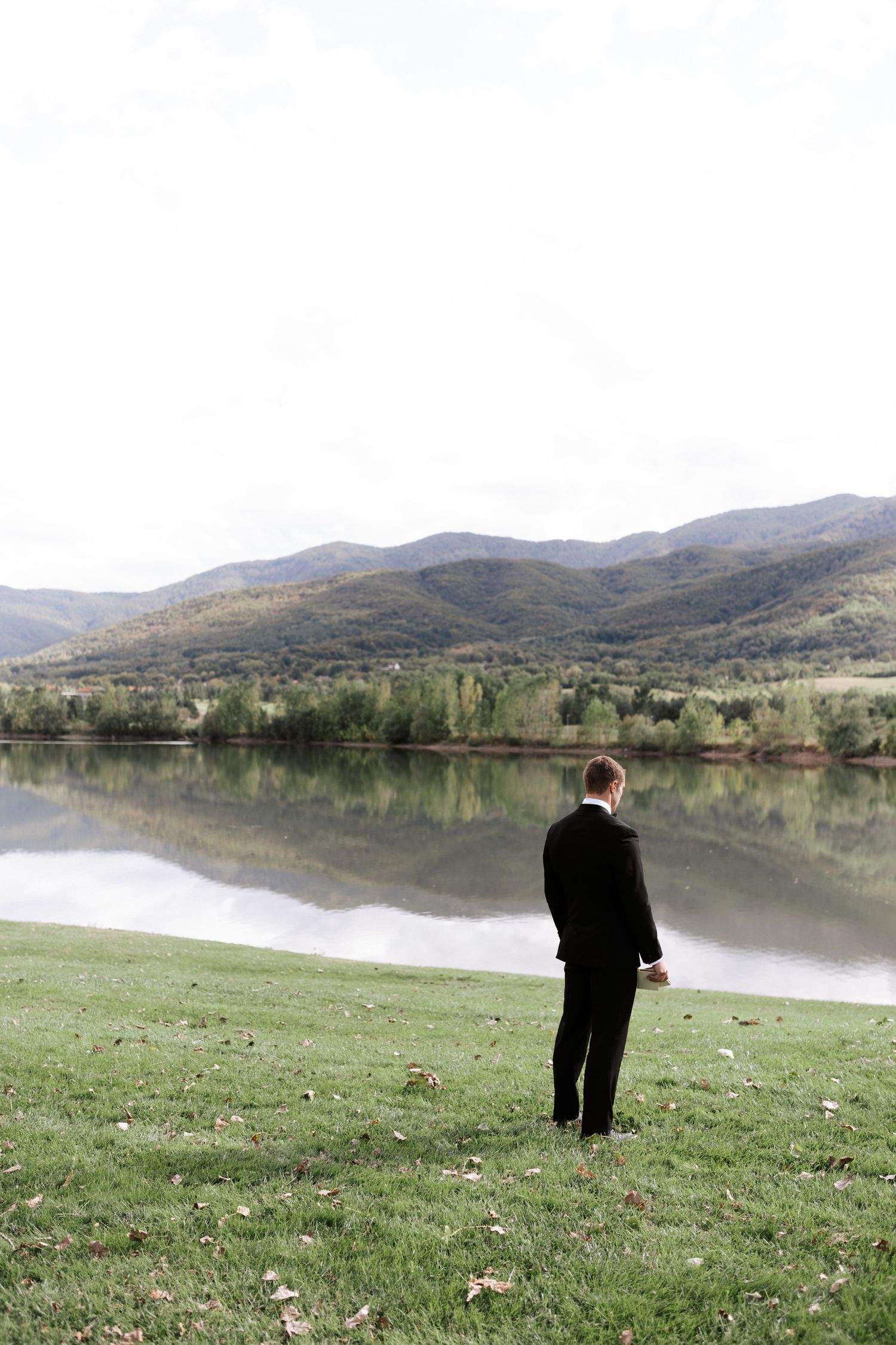 Person in formal attire gazing at a peaceful mountain lake reflection.