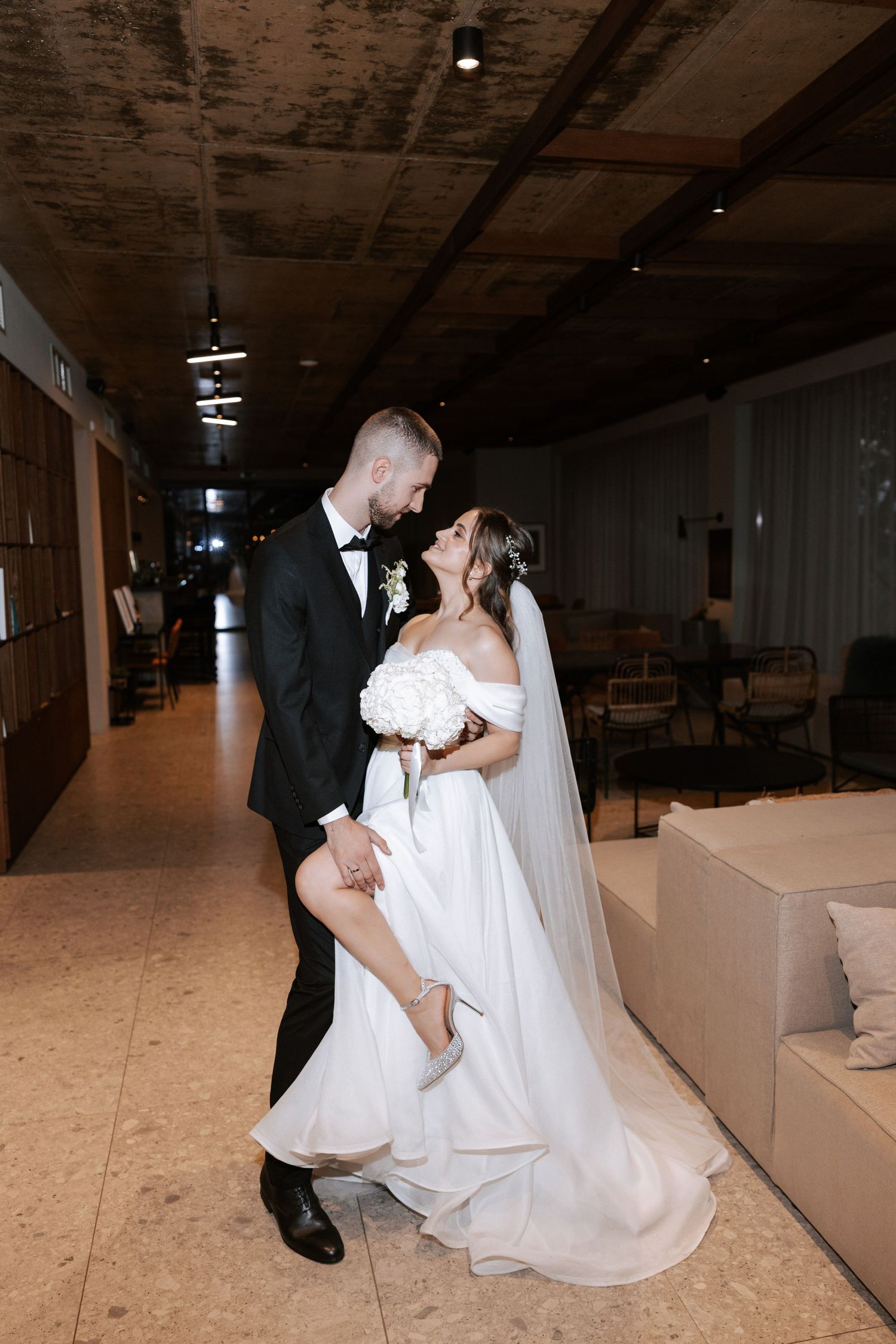 Romantic indoor wedding photo with couple in playful dancing pose.