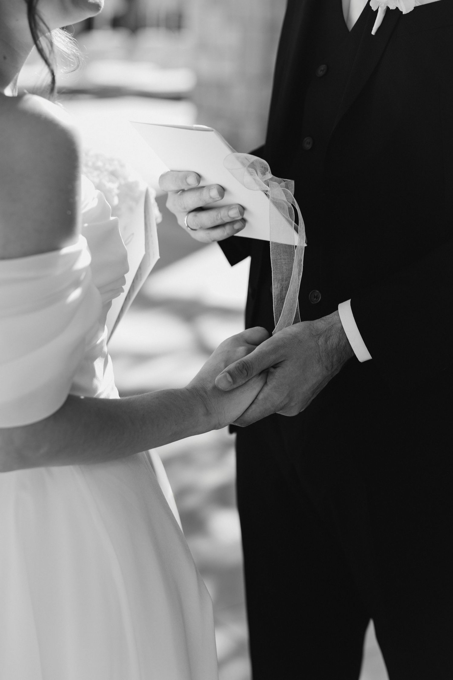 Black and white close-up of wedding couple's hands during vow exchange.