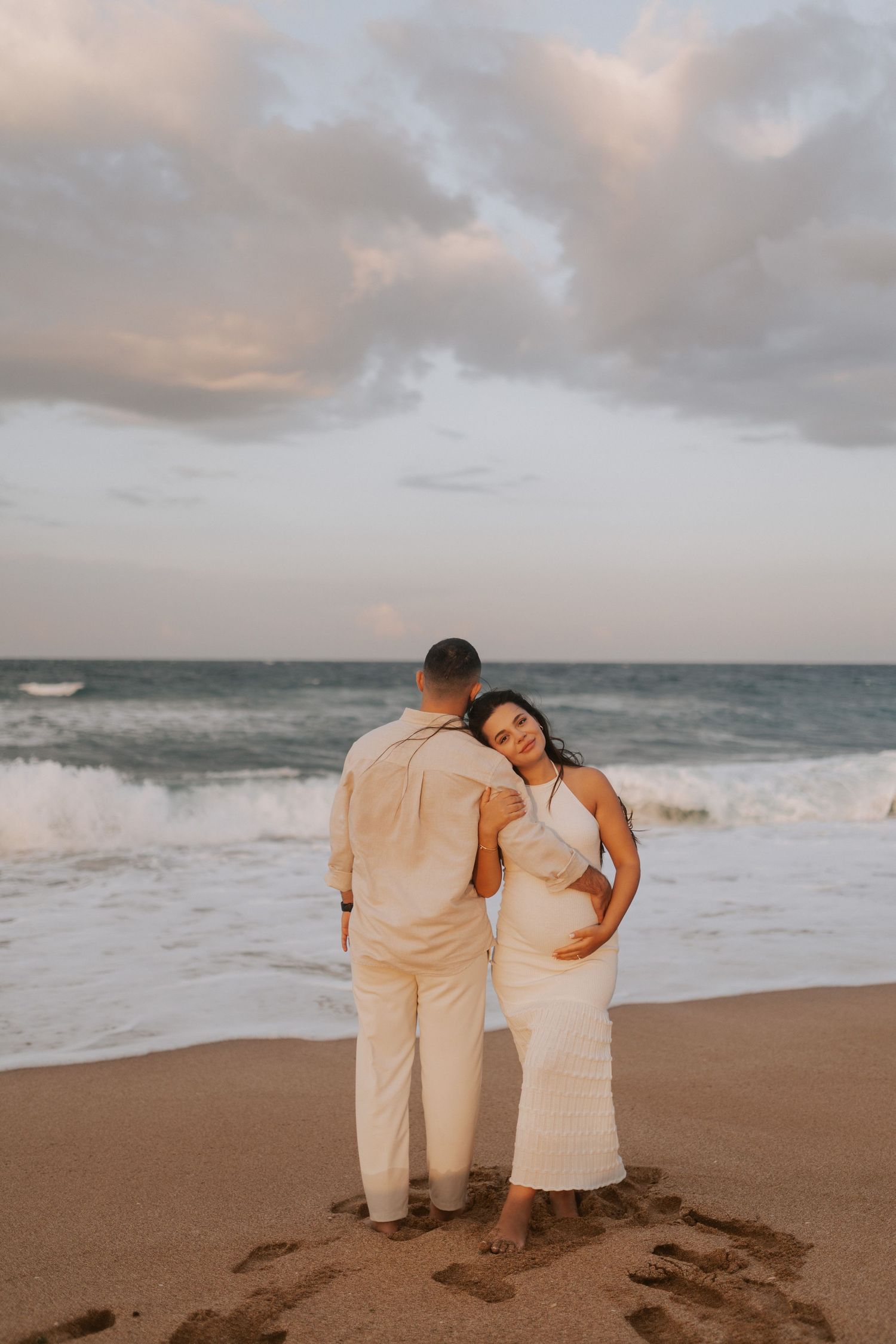 A couple shares a tender moment on the beach with ocean waves crashing behind them.