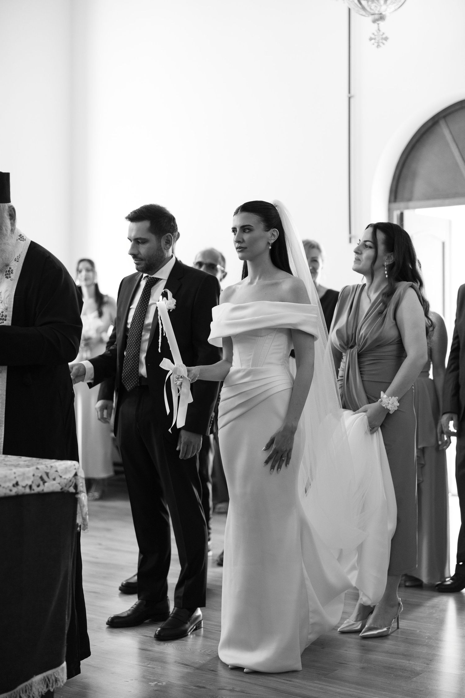 Black and white wedding reception photo showing guests mingling and dancing in a bright indoor venue.