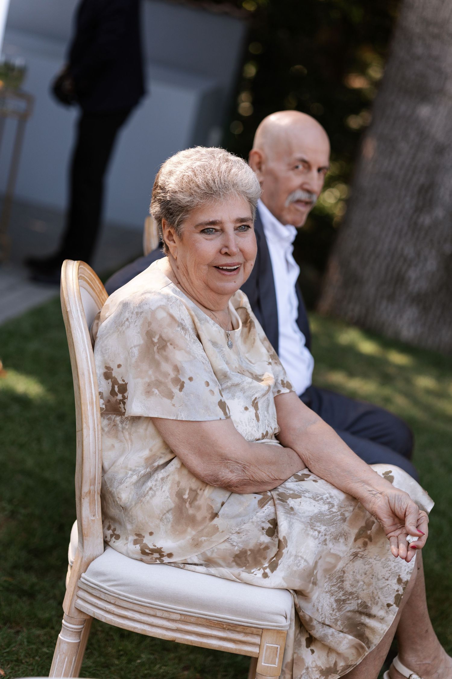 Guest in a floral dress sits in an elegant chair at an outdoor wedding celebration.