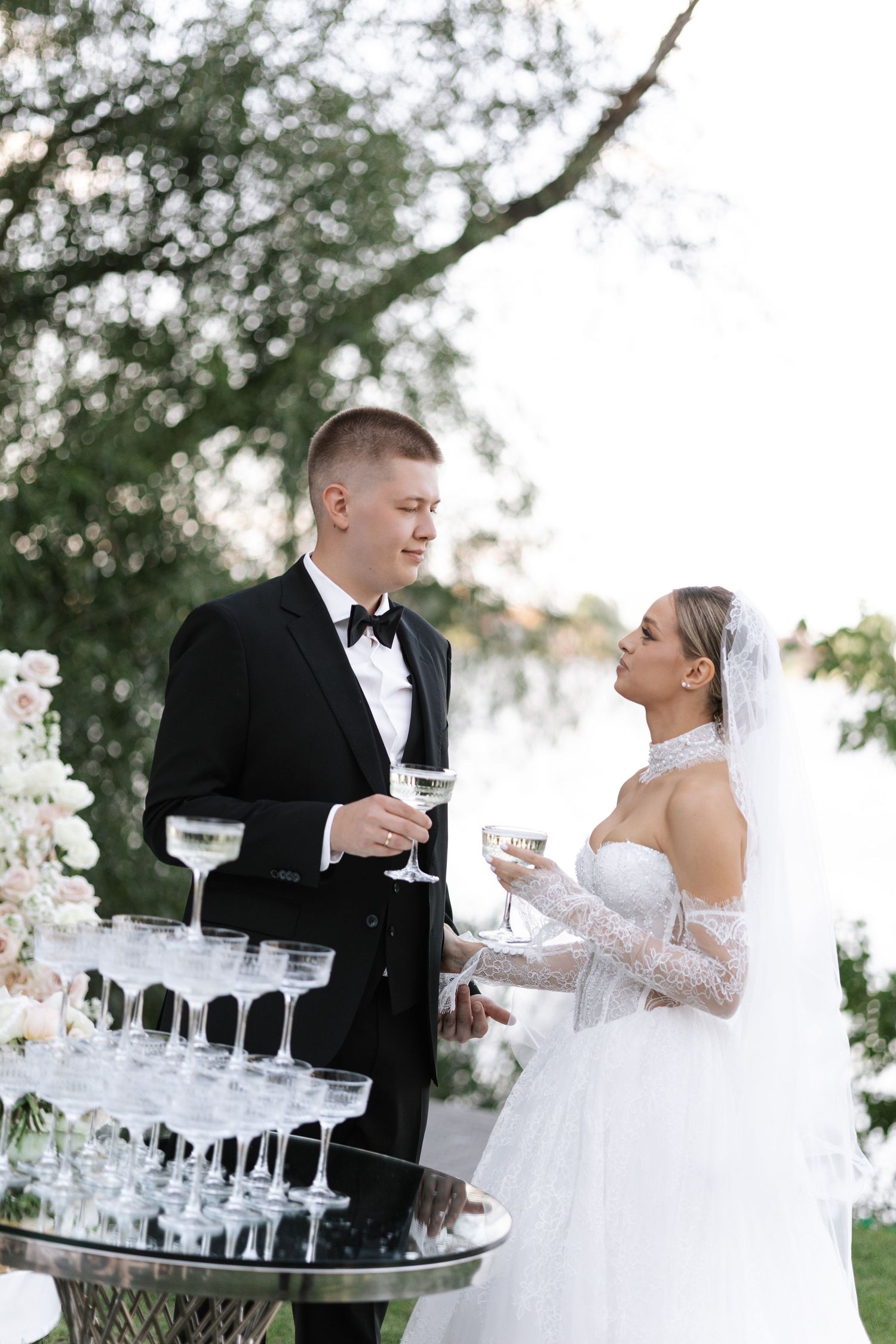 A wedding couple shares champagne outdoors with a tray of elegant glasses.