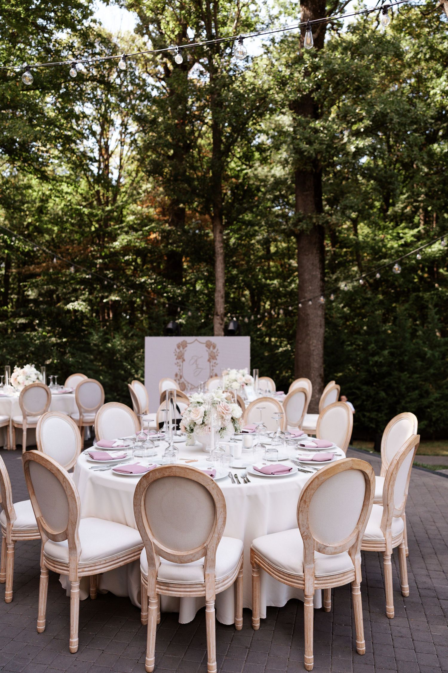 Elegant outdoor wedding reception setup with white tables and French provincial chairs.