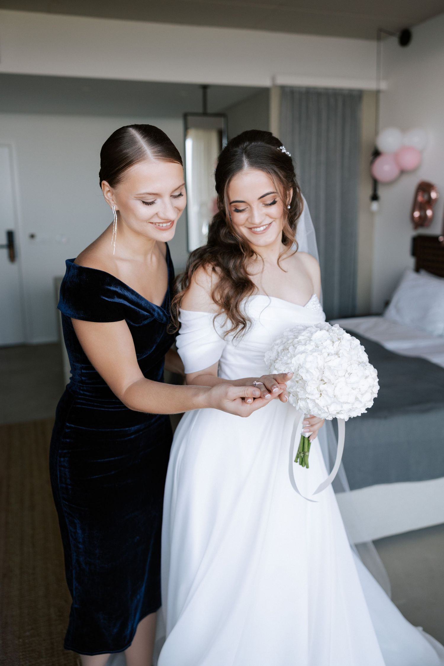 Bride in white gown holding white floral bouquet with bridesmaid in navy velvet dress.