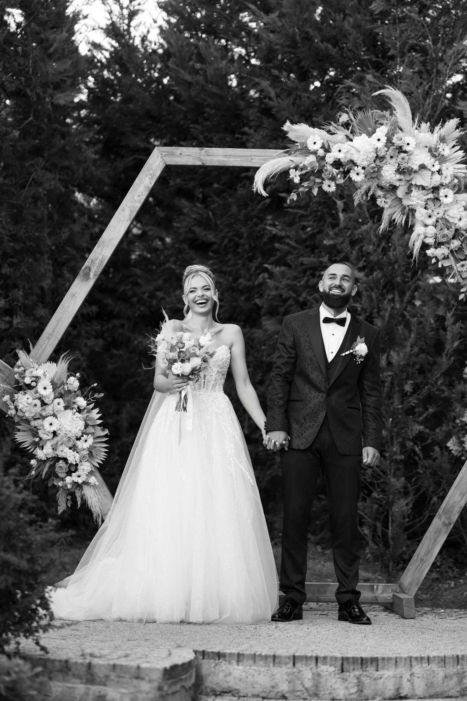 Black and white wedding photo series showing couple in formal attire posing outdoors with floral arrangements and white decor.
