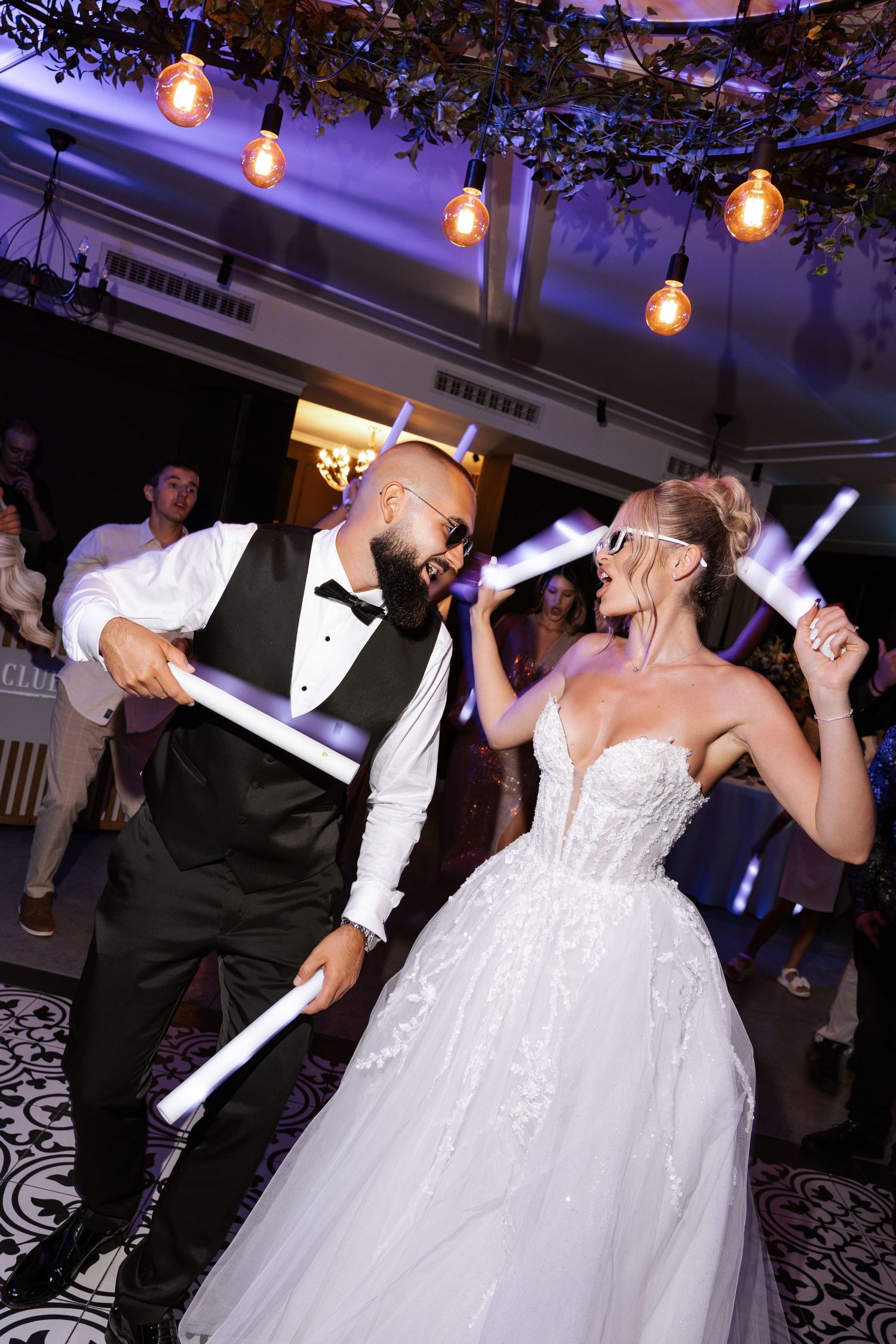 Wedding couple dances together on a decorated dance floor under hanging string lights during their reception celebration.