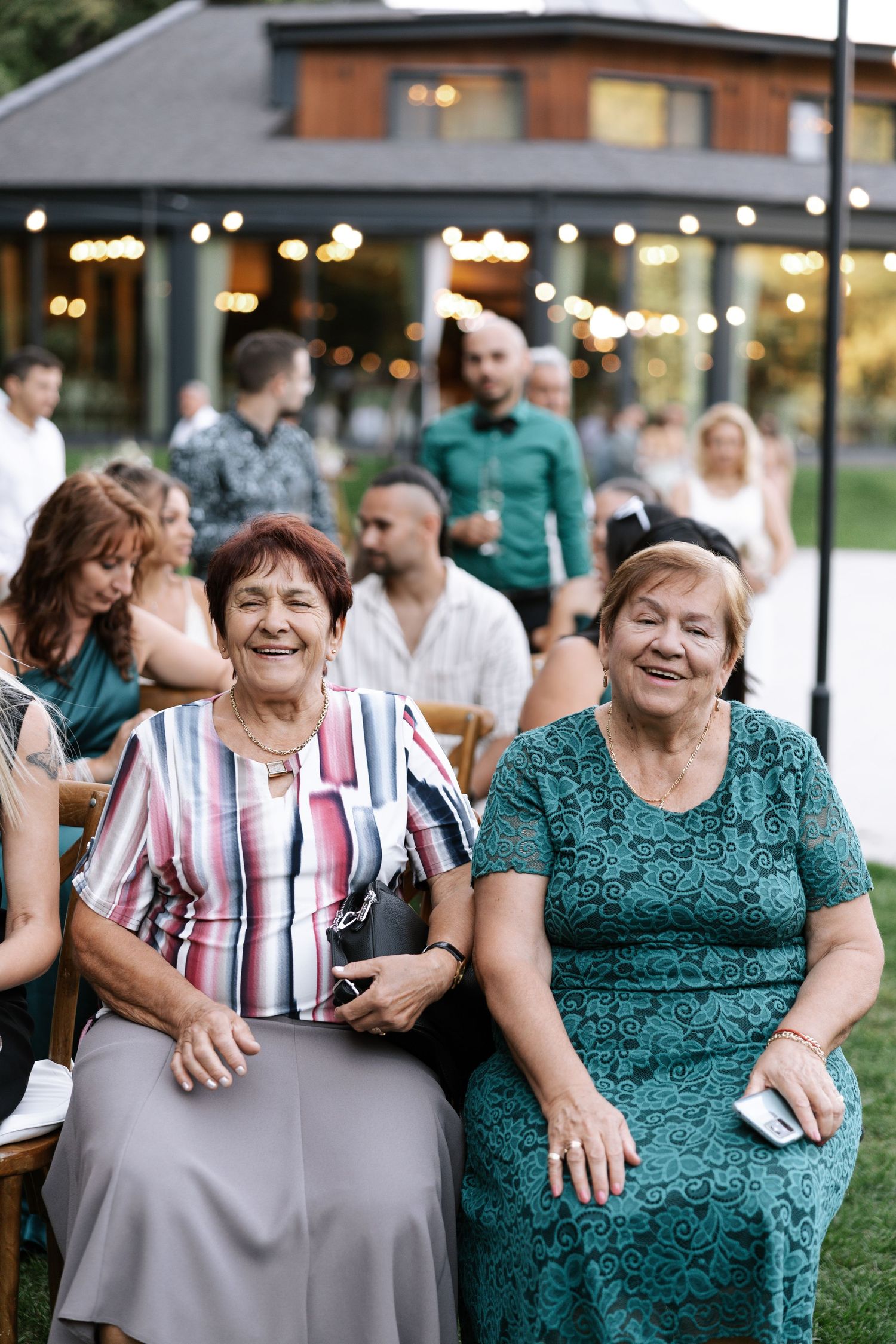 Wedding guests in colorful attire share joyful laughter at an outdoor reception venue.