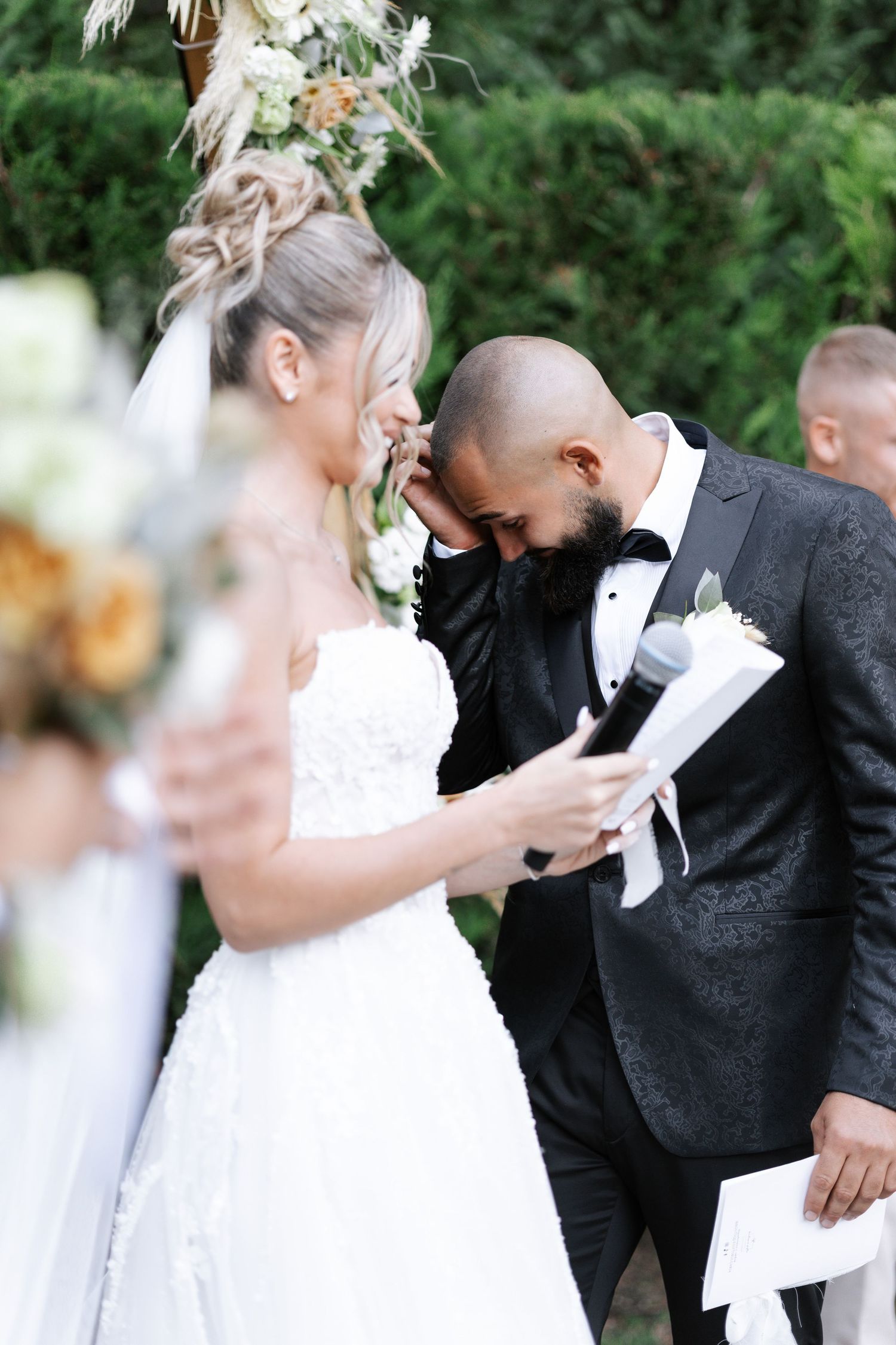 A couple shares an emotional moment while reading their vows during an outdoor wedding ceremony.