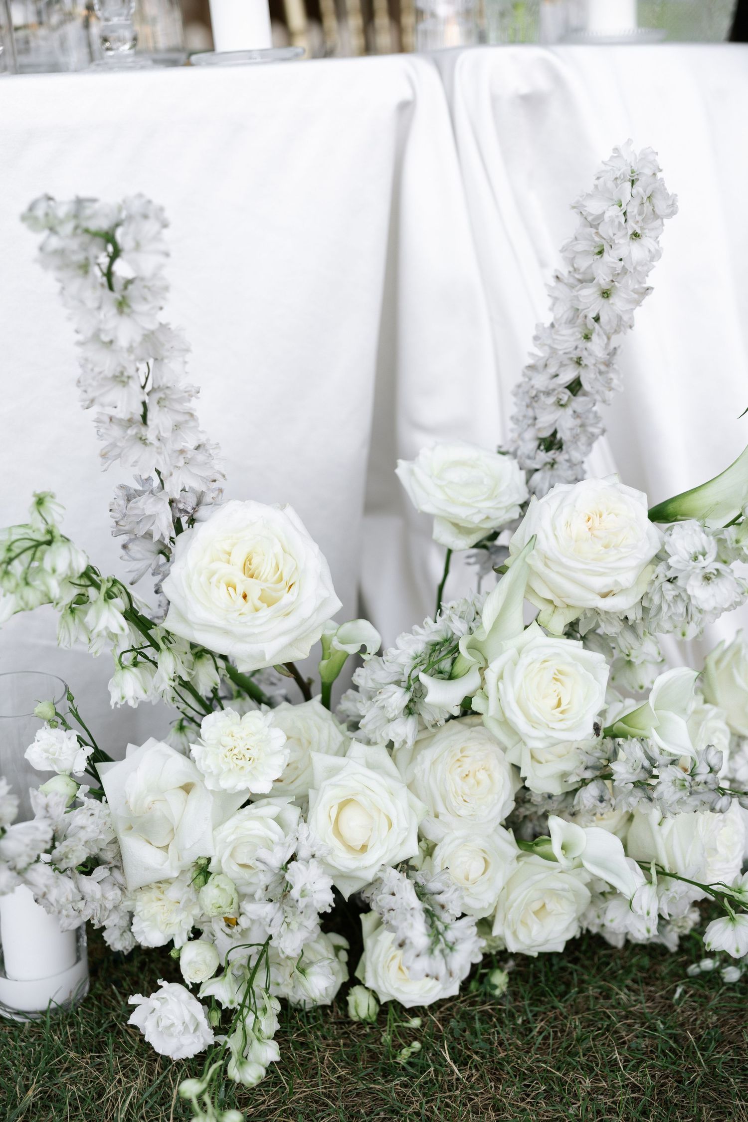 Elegant white roses and delicate floral arrangements cascade along green grass creating a romantic garden border display.