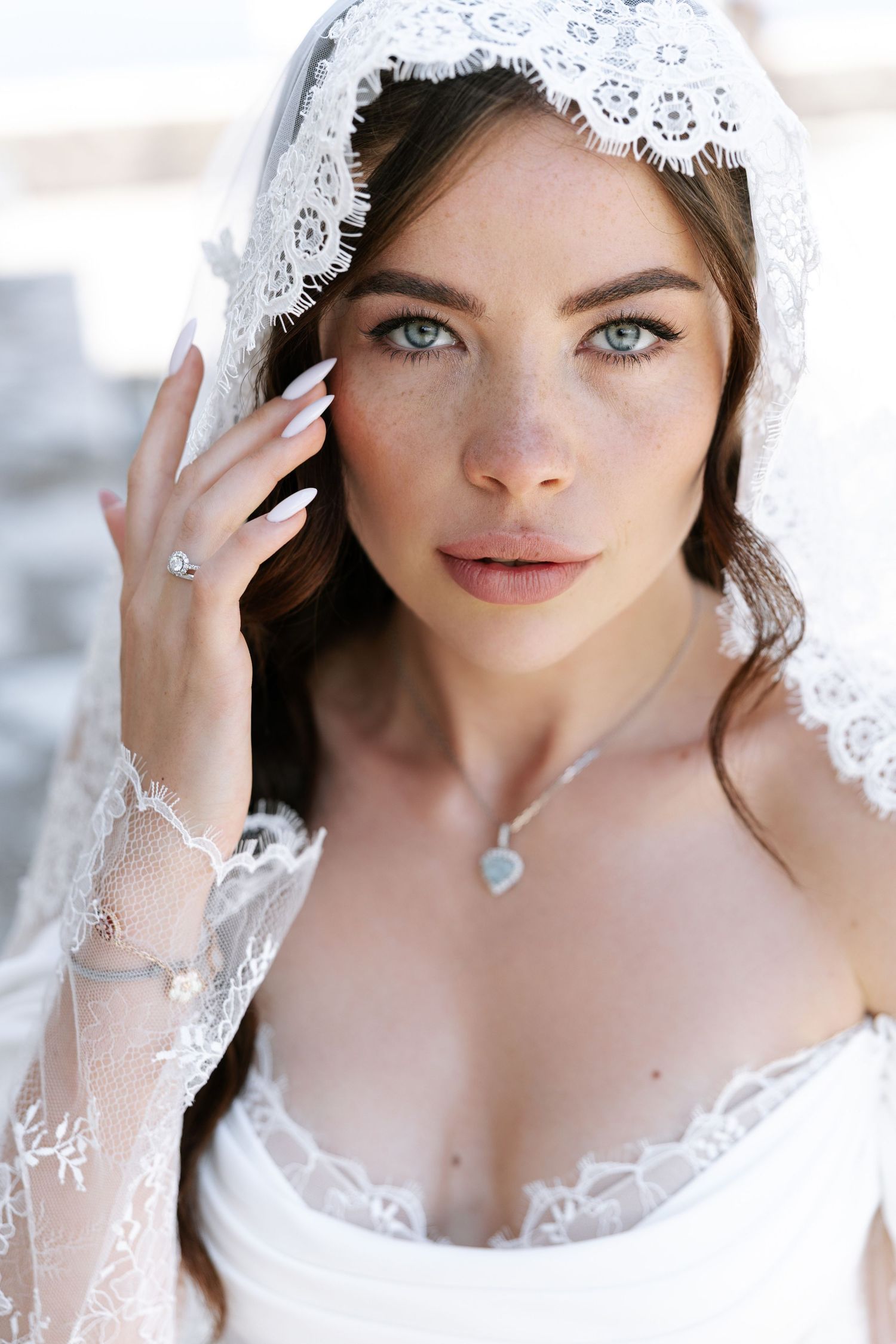 Close-up bridal portrait with delicate white lace veil and heart-shaped necklace in soft natural lighting.