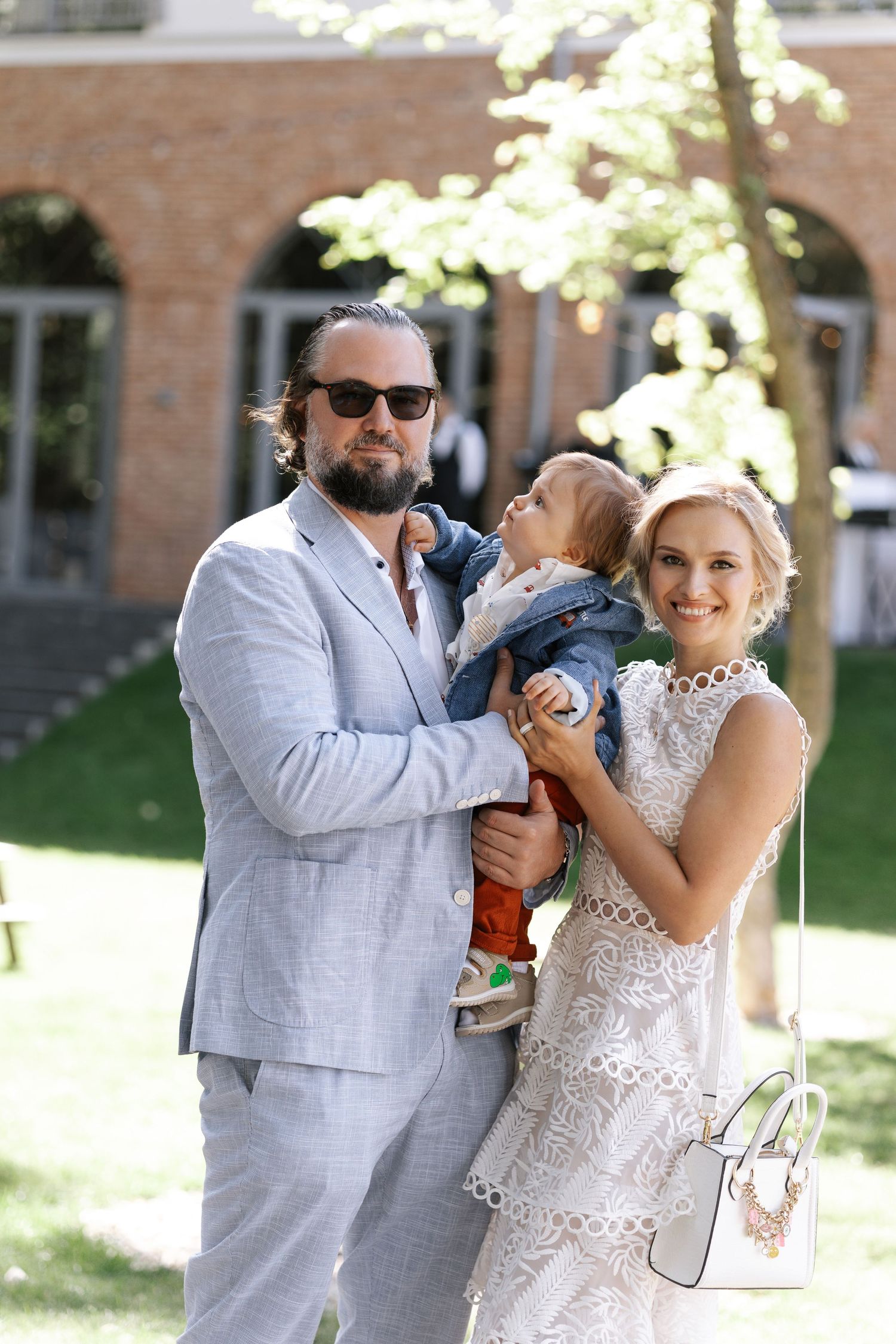 Wedding couple shares playful moment outdoors in front of brick building on sunny day.