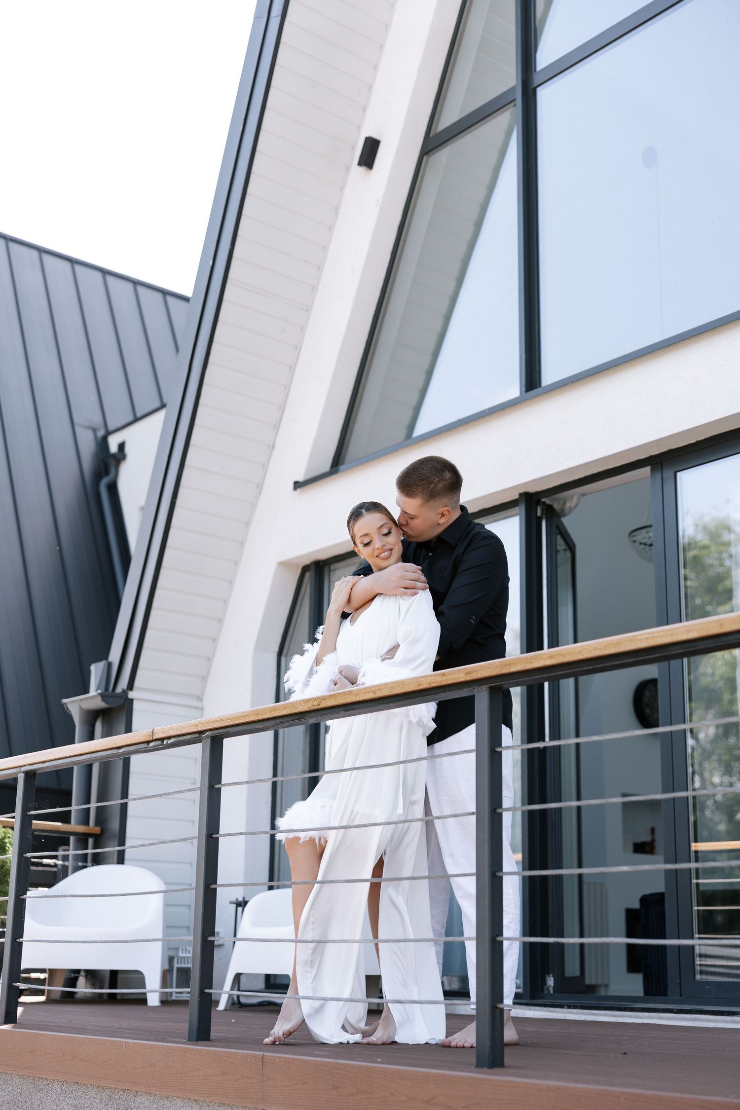 Couple in matching white outfits sharing a moment on an outdoor balcony.