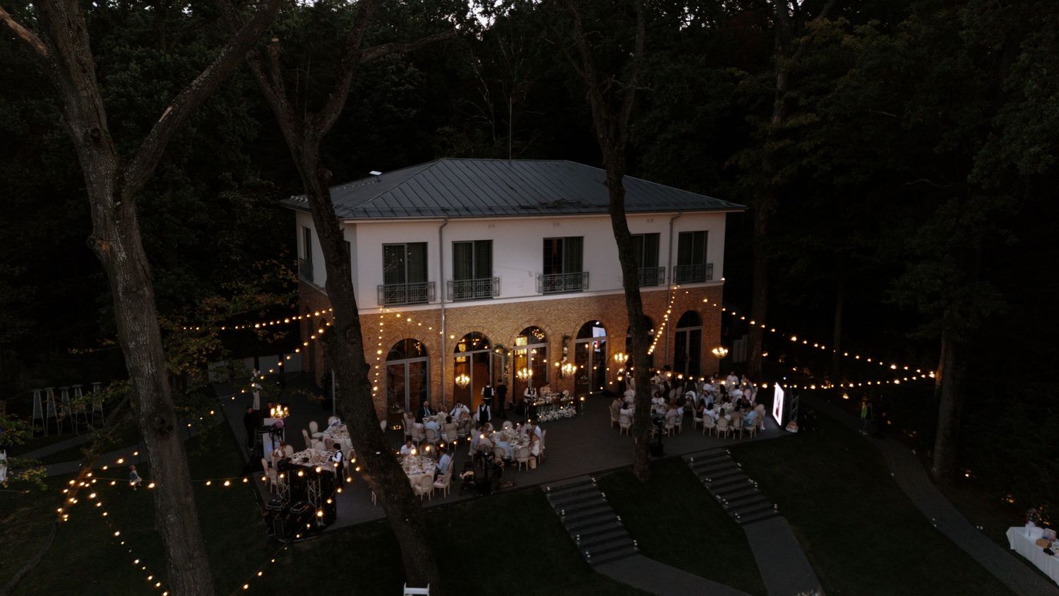 An evening view of an elegant wedding venue with twinkling lights and arched windows.