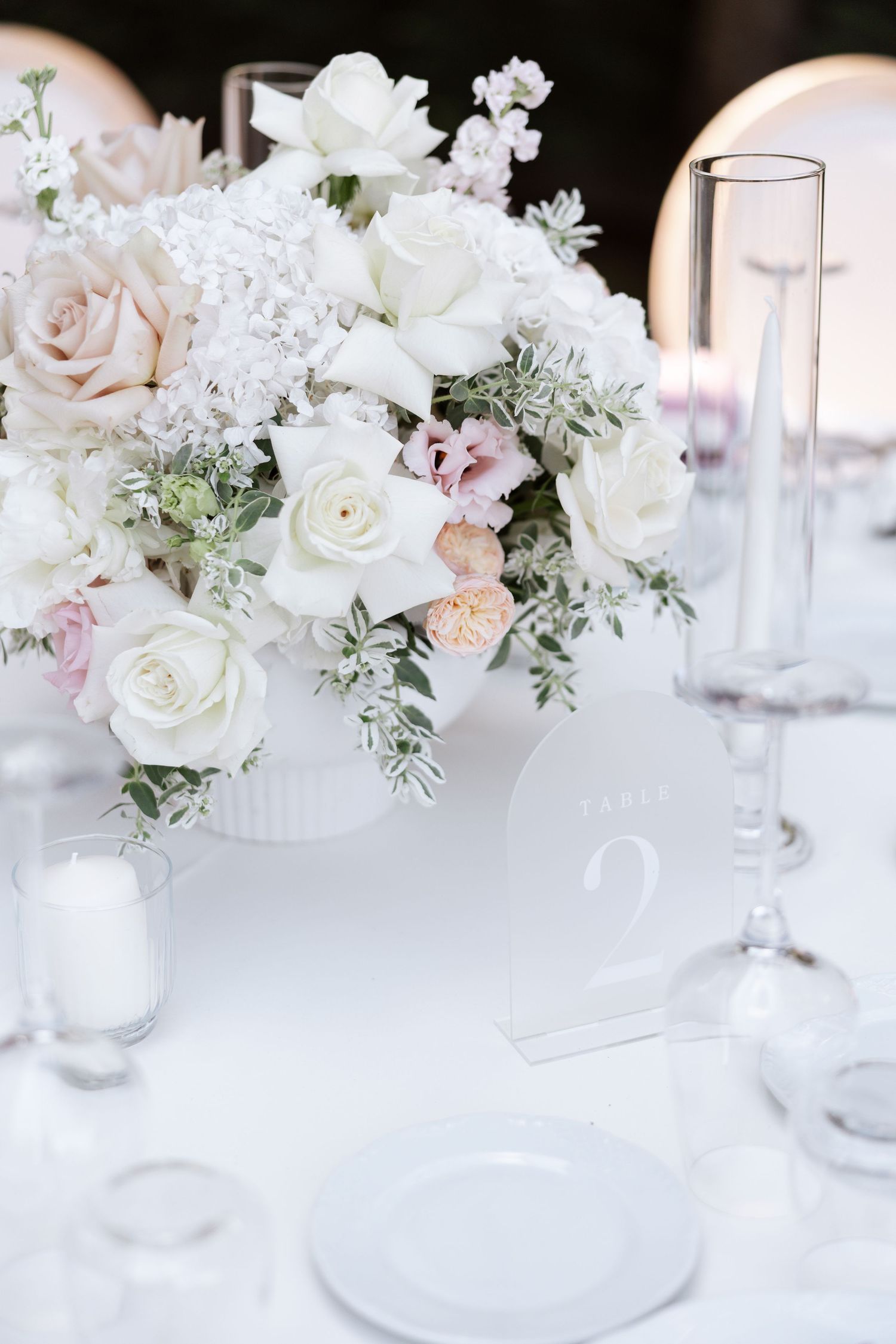 Elegant white and blush floral centerpieces with roses and greenery on wedding reception tables.