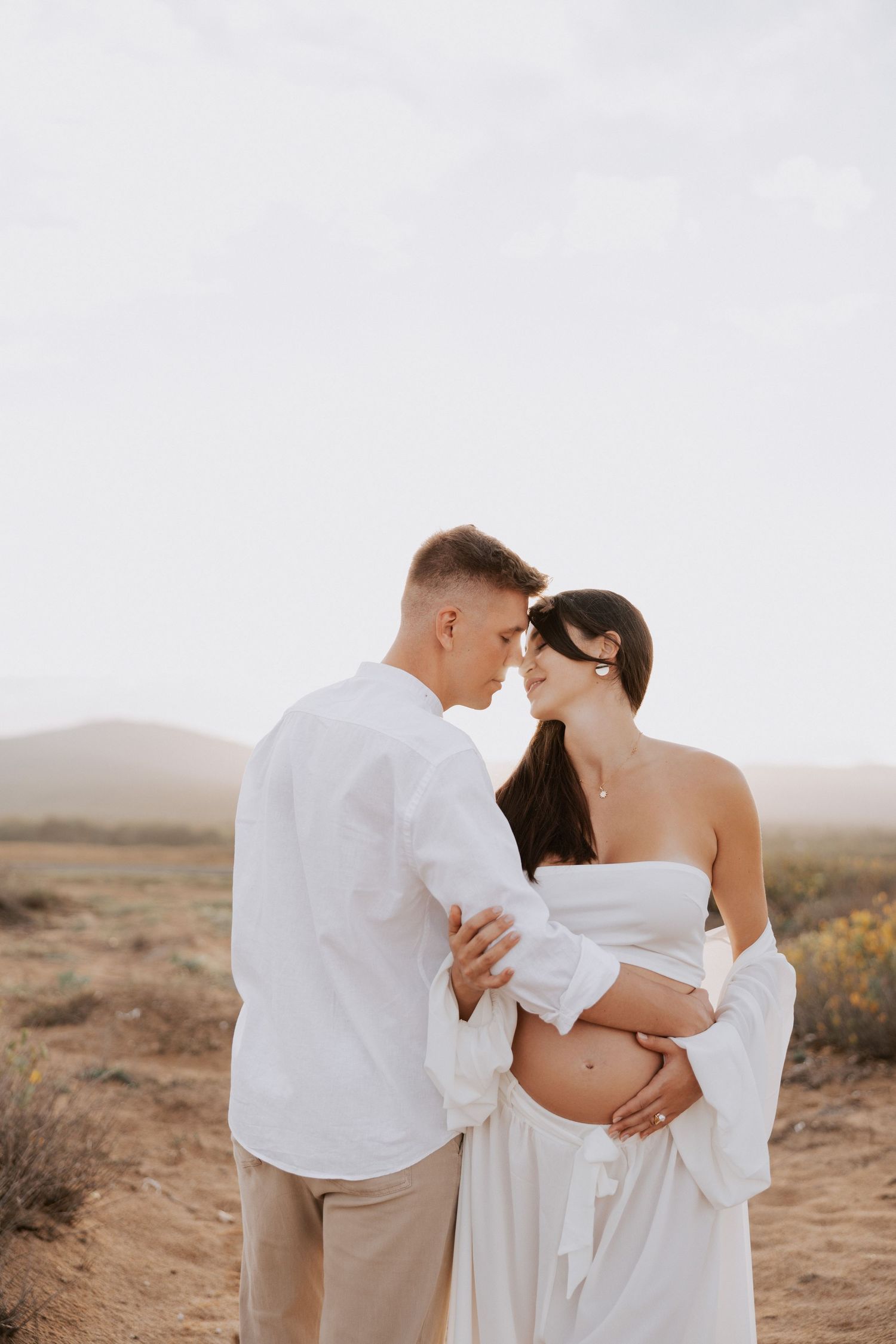 Intimate moment between couple in white clothing against desert backdrop.