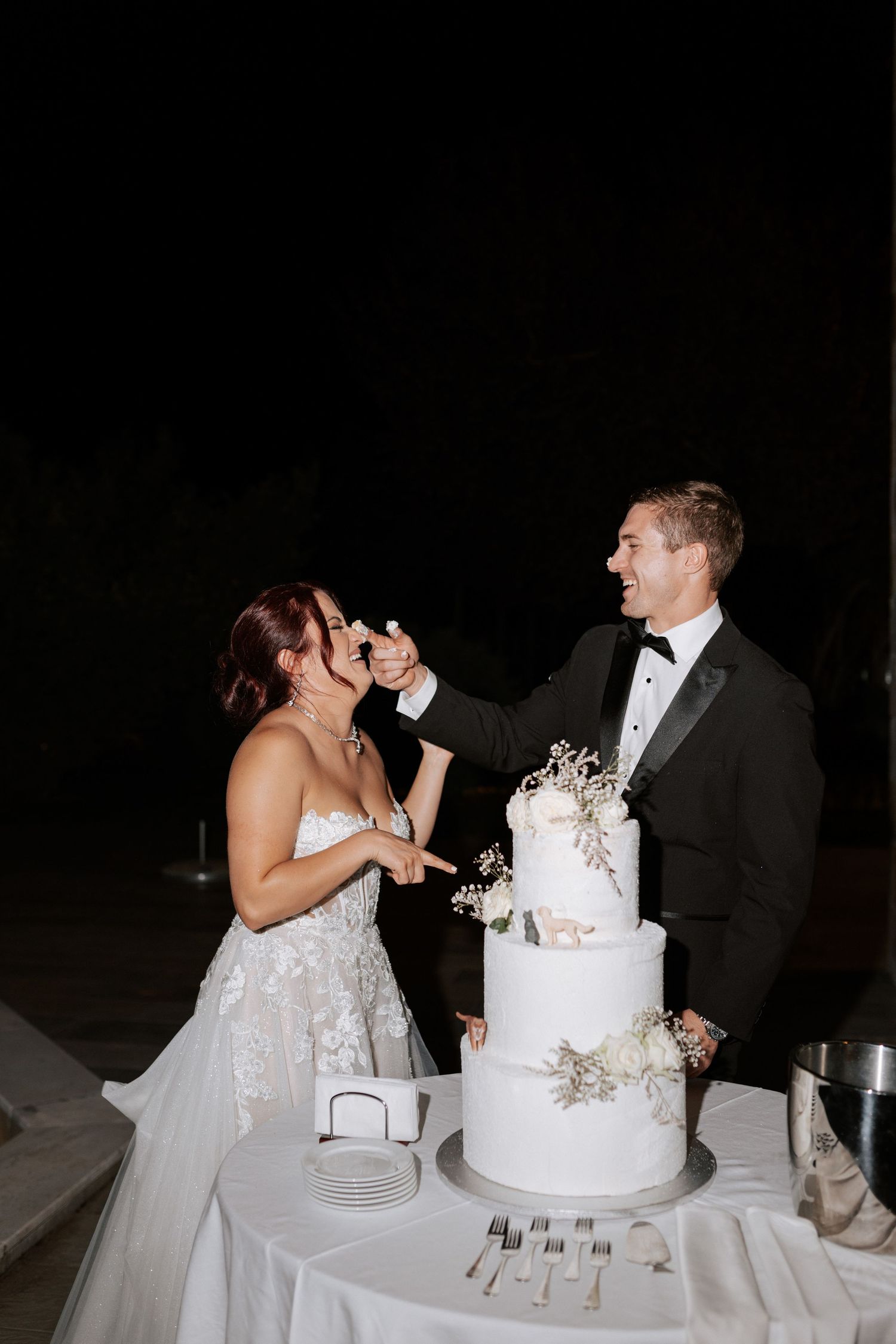 Playful cake cutting moment at wedding reception with elegant white tiered cake.Wedding photographer Bulgaria