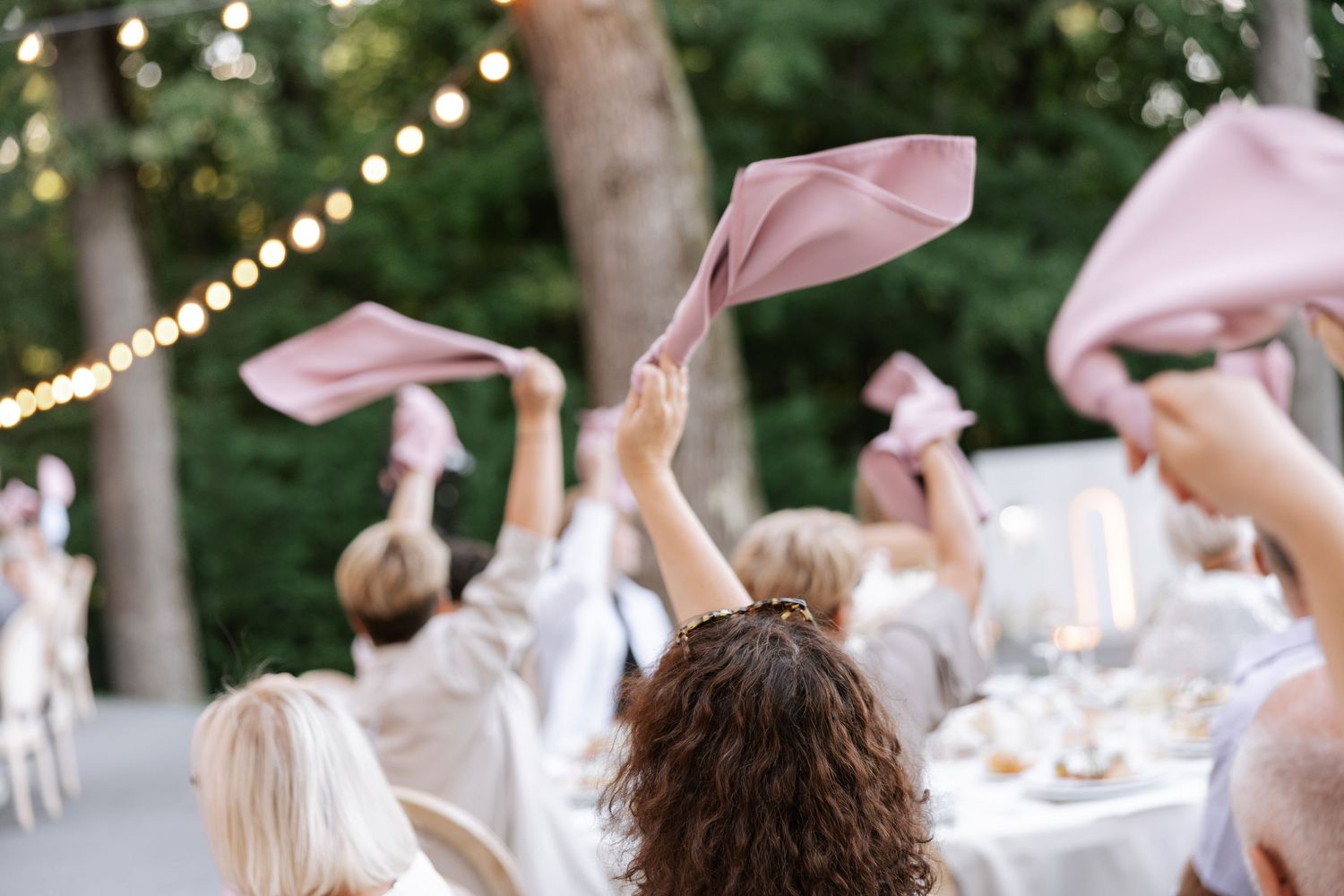 Wedding celebration with guests waving napkins in outdoor setting.