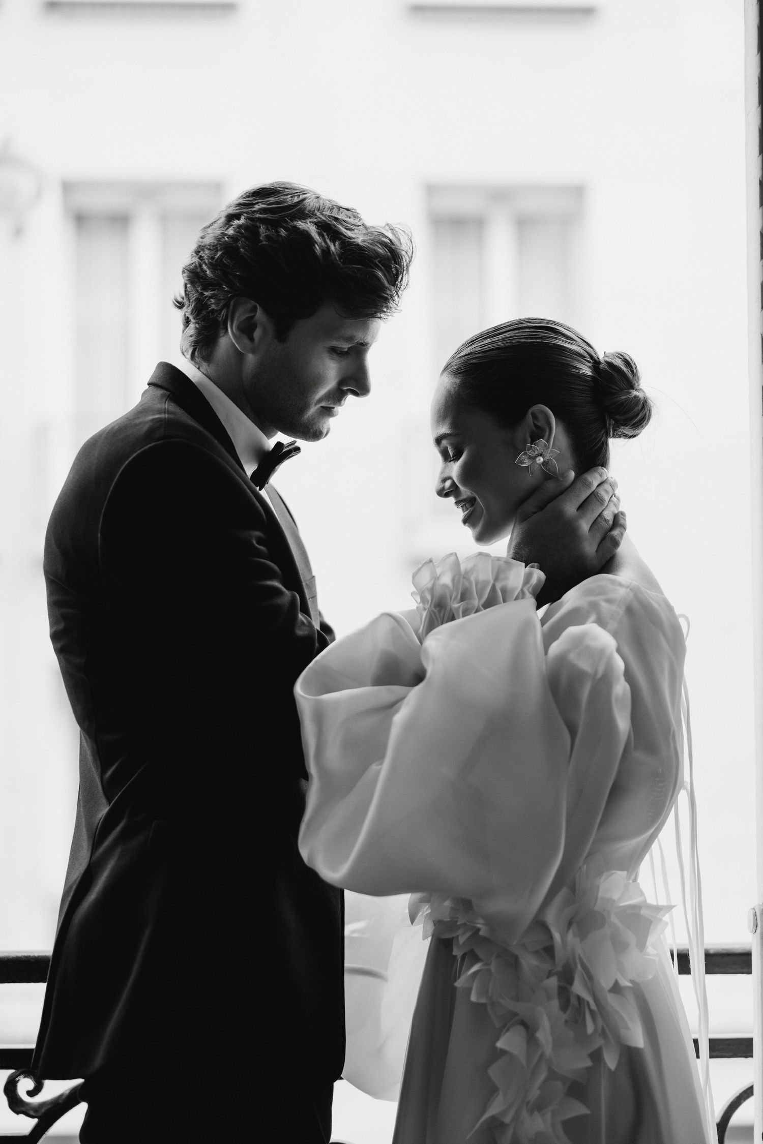 A romantic black and white photo of a couple in formal wear sharing an intimate moment on a balcony.
