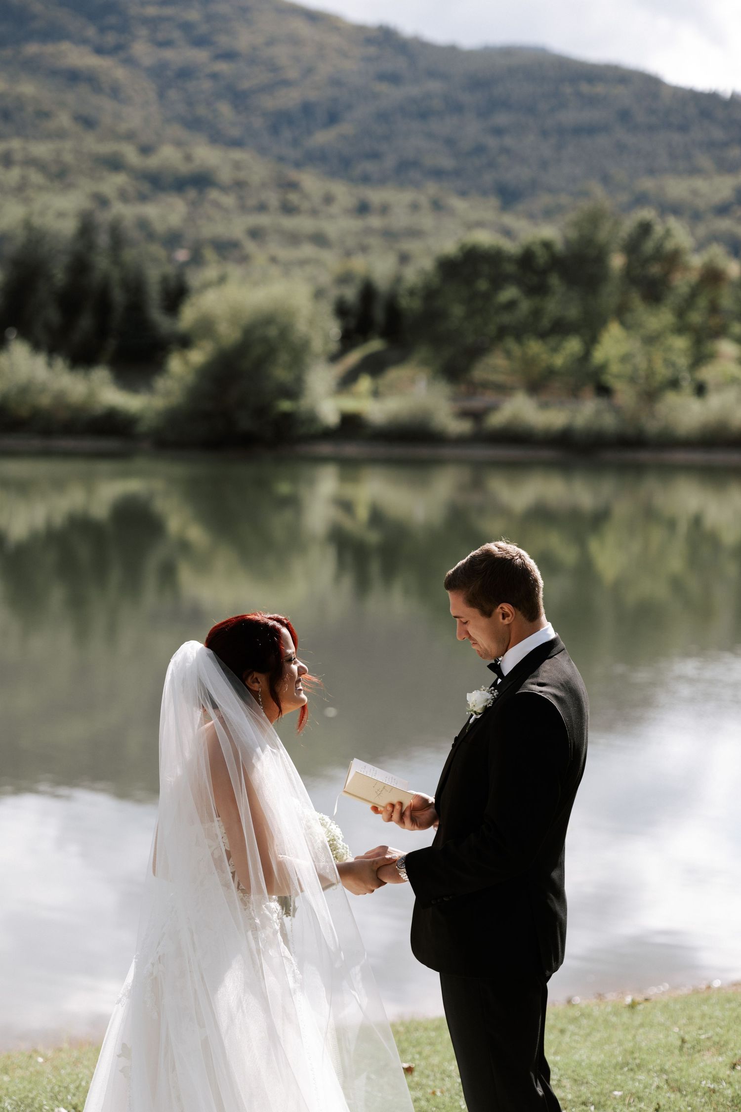 Couple exchanges vows during their lakeside wedding ceremony against a mountain backdrop.