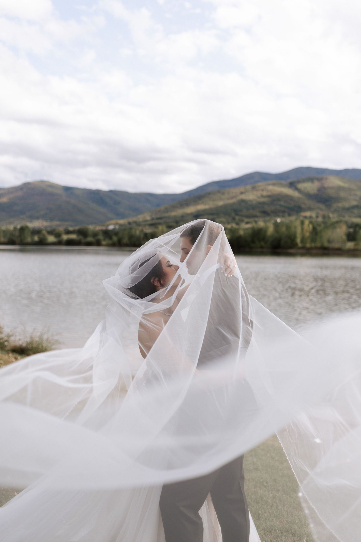 Flowing white wedding veil catches the breeze against a mountainous lake landscape.