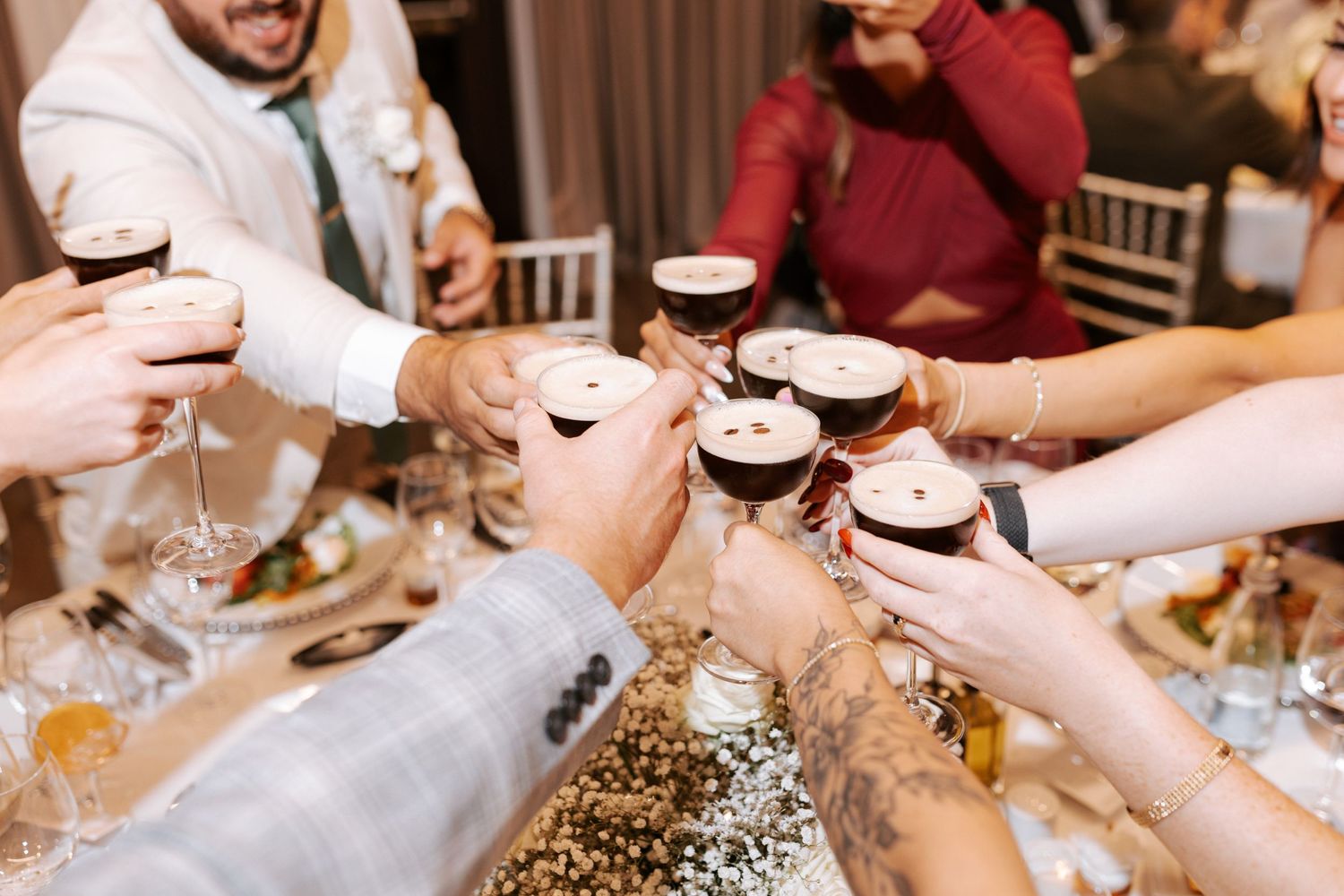 Guests toasting with dark drinks at a wedding reception with glittery tablecloth.