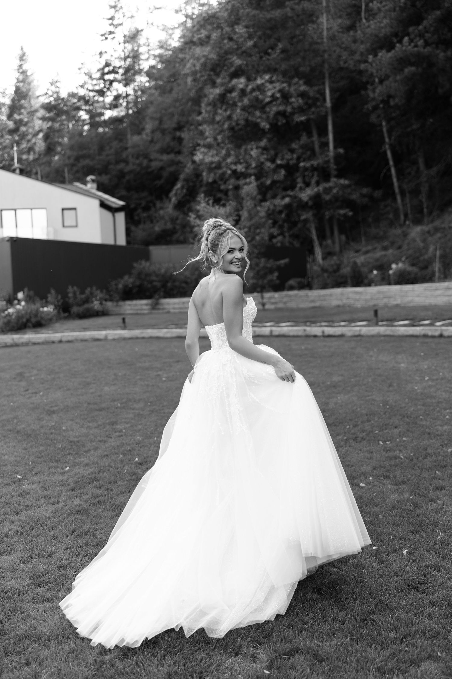 A bride in a flowing white ballgown twirls gracefully across a grassy field on a summer evening.