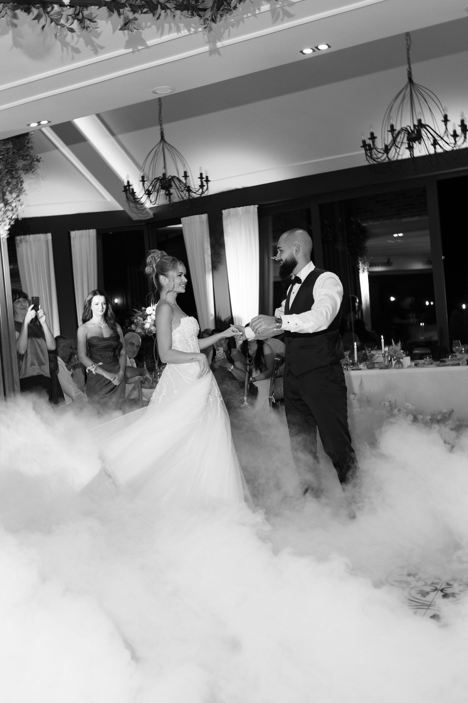 A couple dances their first dance as newlyweds on a fog-covered dance floor at an elegant wedding reception.