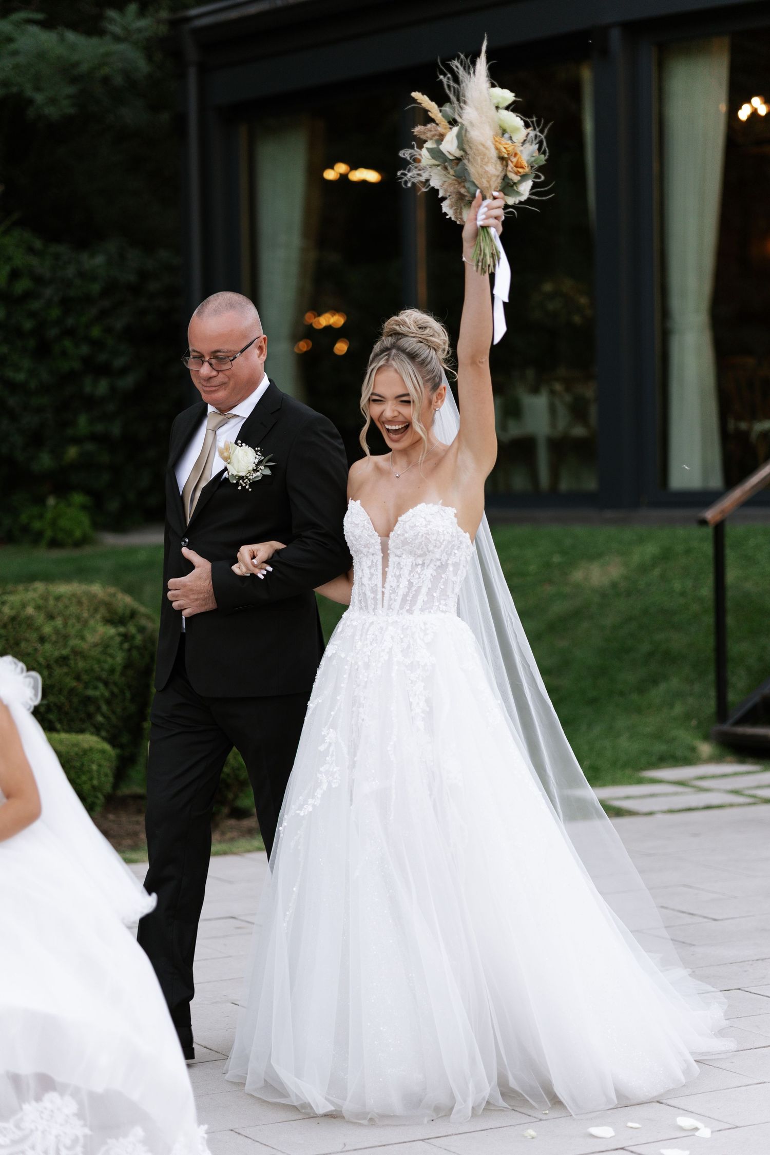A newlywed couple dances and spins together outdoors, with the bride in a flowing white gown and the groom in a black suit.