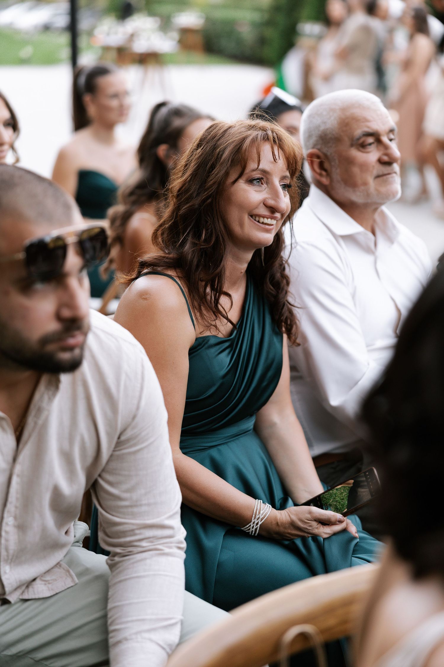 A group of wedding guests in white and teal attire smile and laugh during an outdoor celebration.
