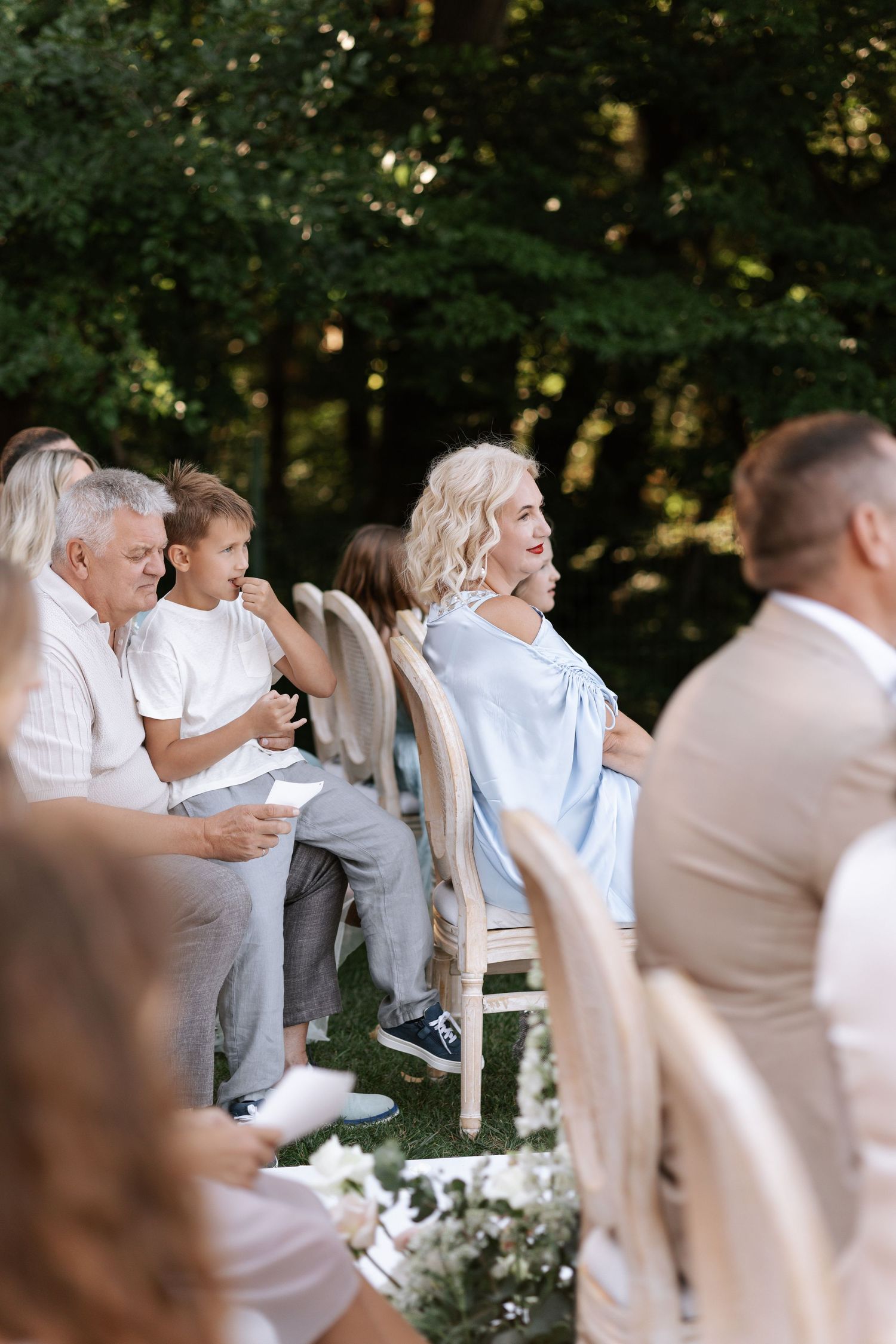 Wedding guests in light colored attire celebrate during an outdoor reception.