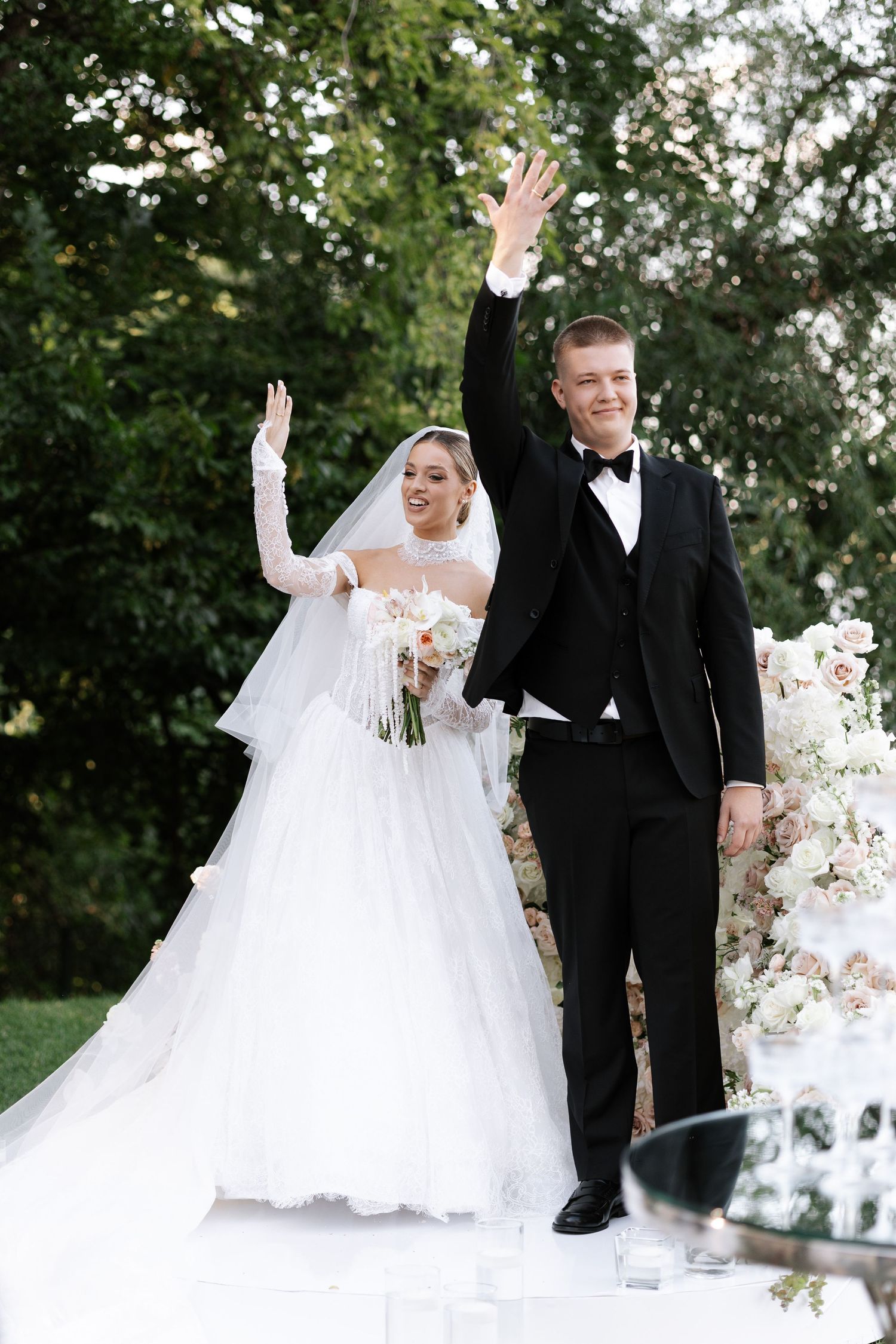 Wedding couple waving and celebrating on their special day outdoors.