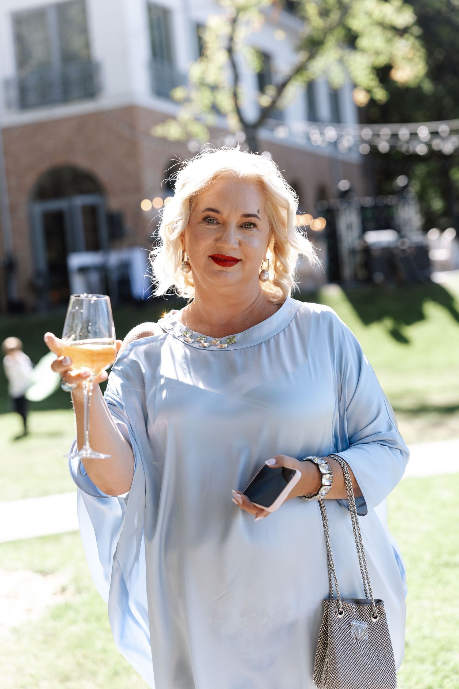 Person in light blue outfit enjoying drinks outdoors on a sunny day.